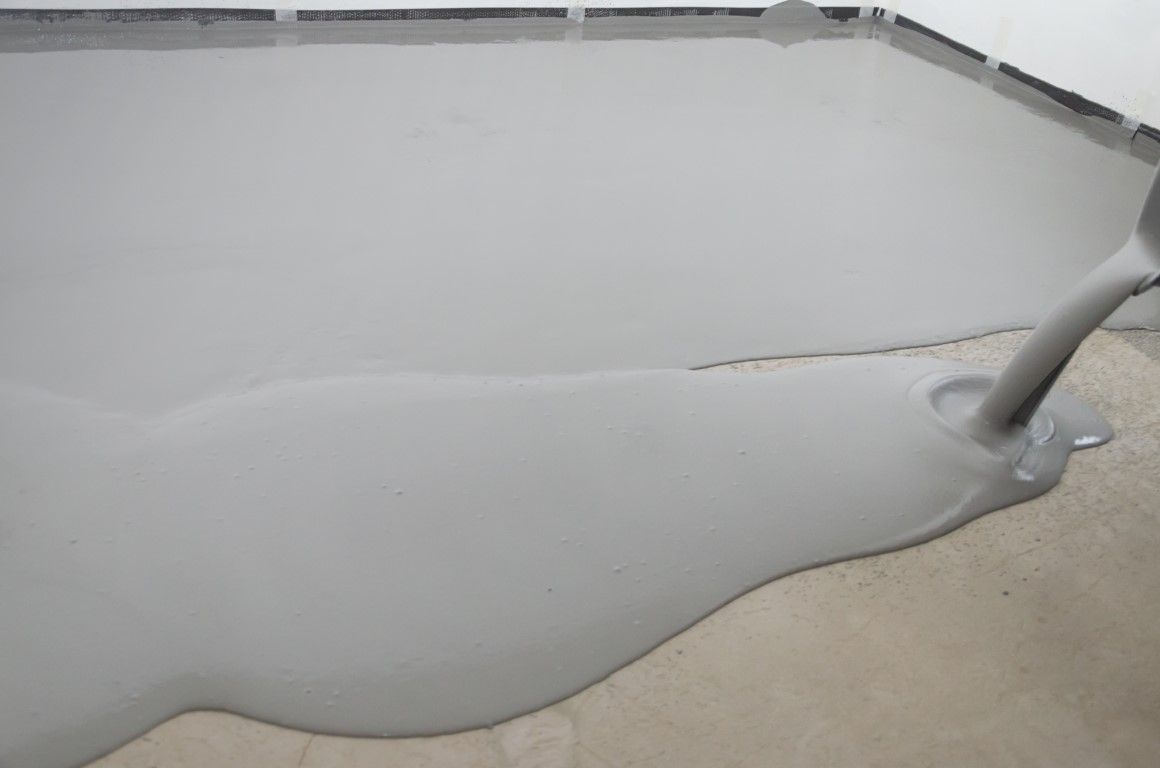 Gray liquid spreading over a concrete floor with a crack and a small pipe at the edge