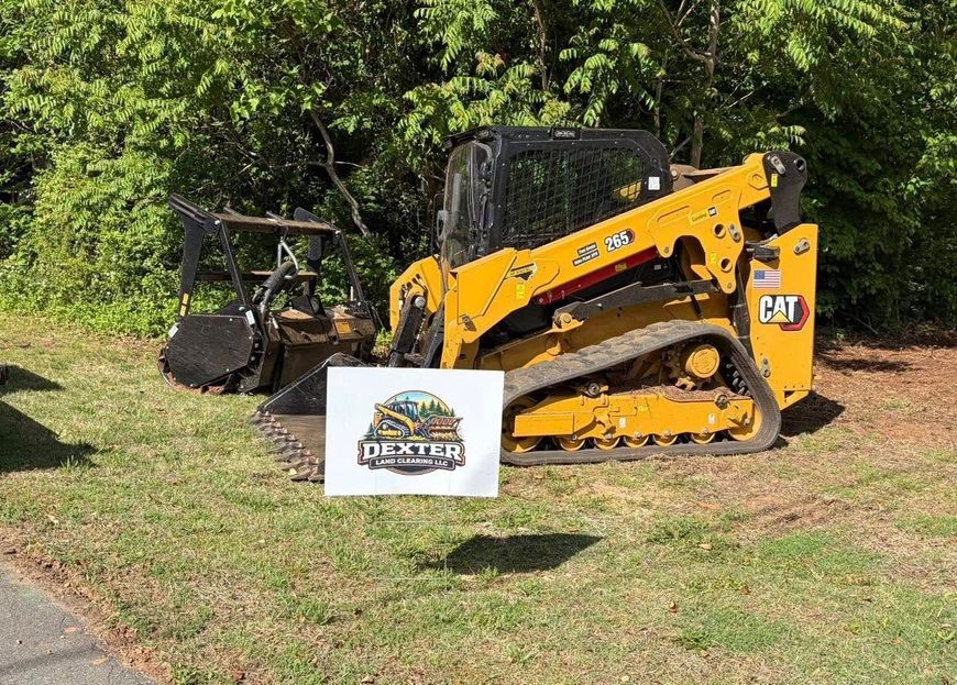 Yellow CAT track loader parked on grass beside a sign, with trees in the background.