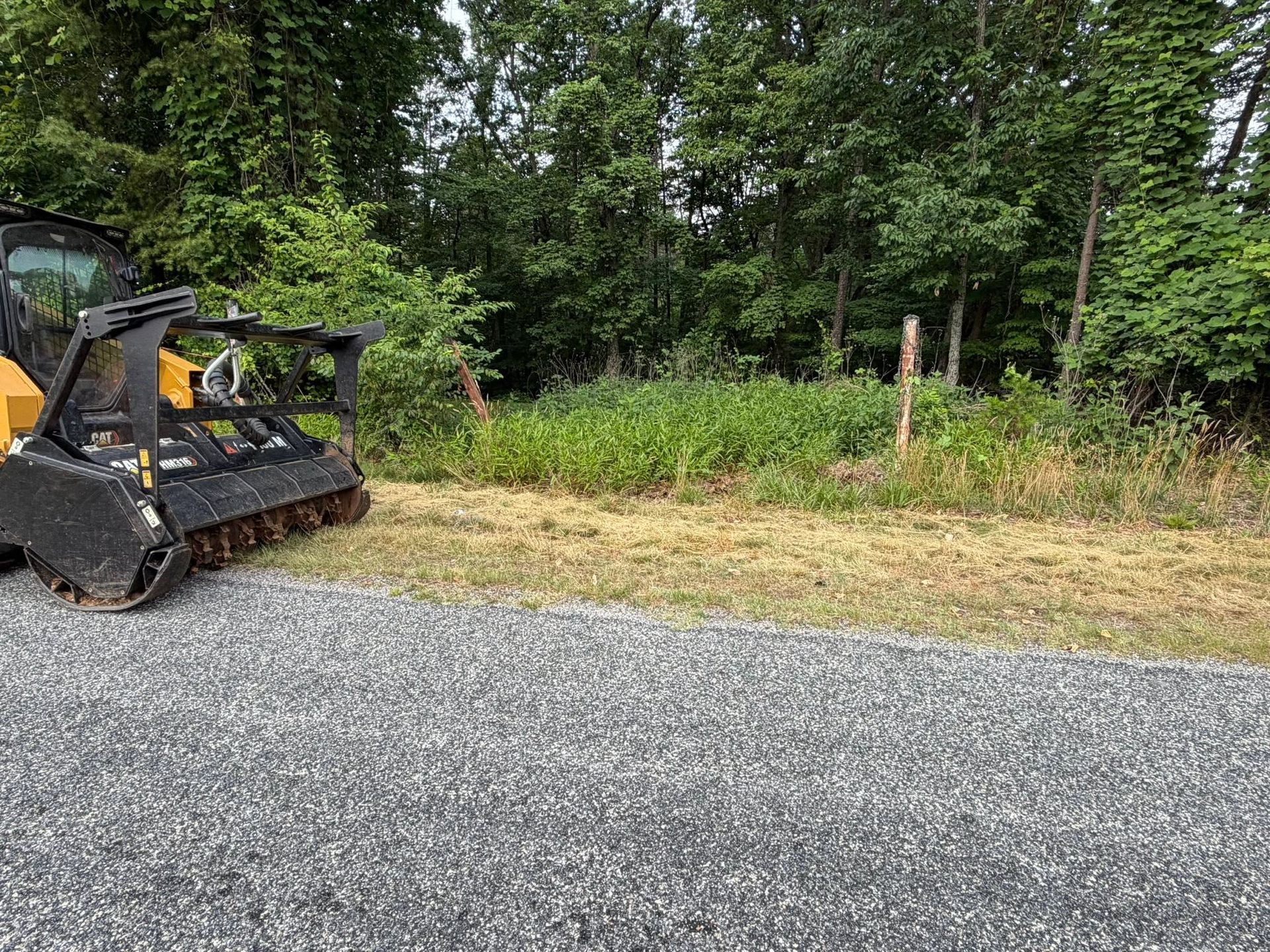 Yellow construction vehicle parked beside a gravel road with trees and brush in the background