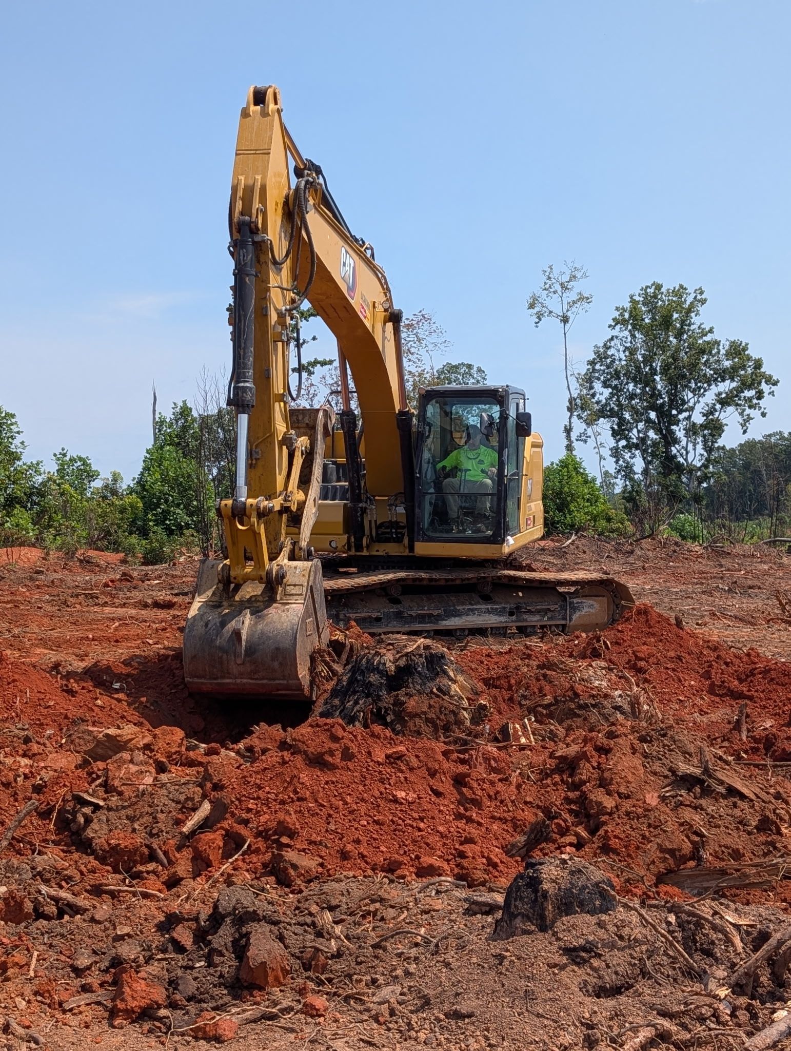 Yellow excavator on red dirt at a construction site under a clear sky