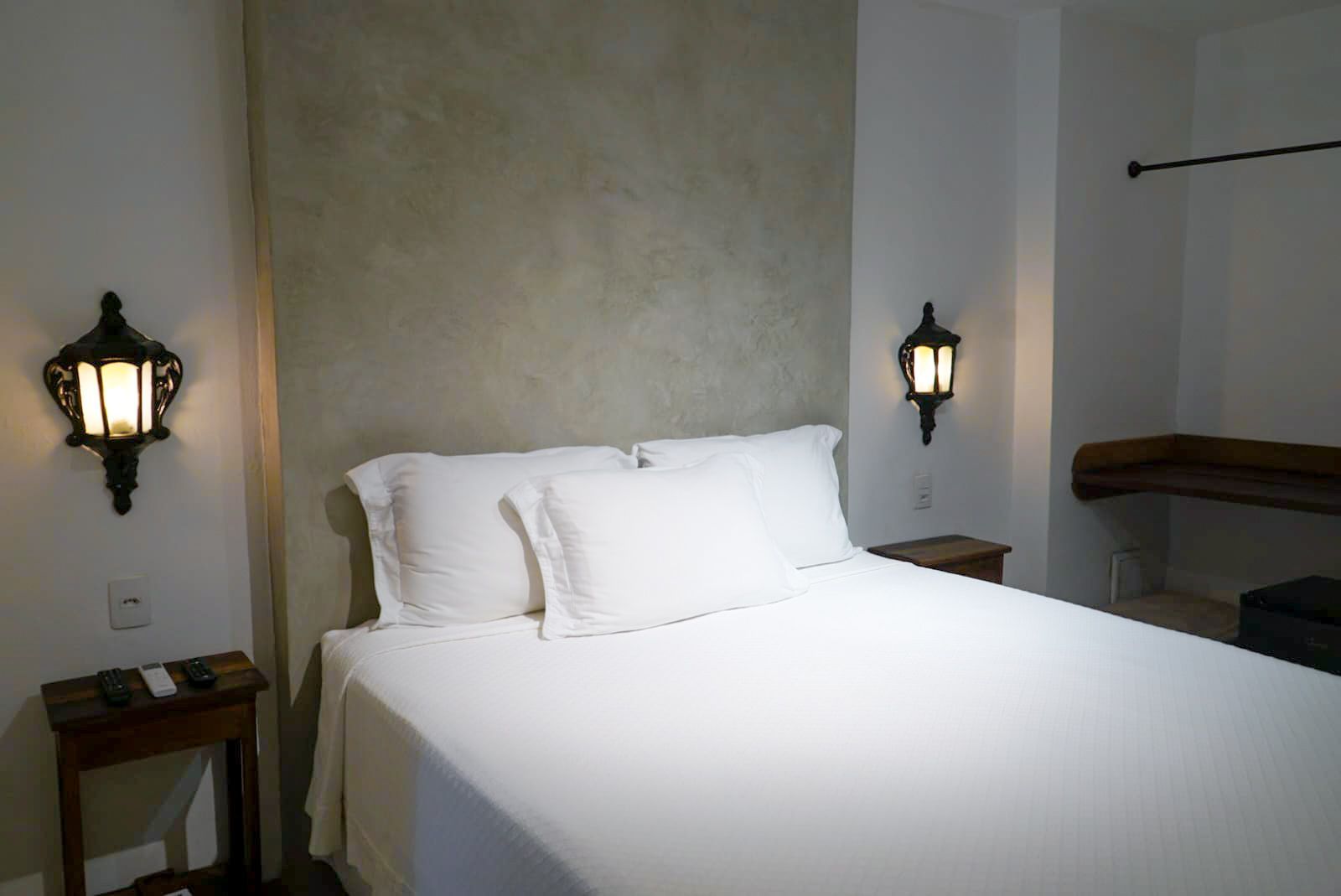 Bedroom with white bedding, side tables, sconces, and a bench.