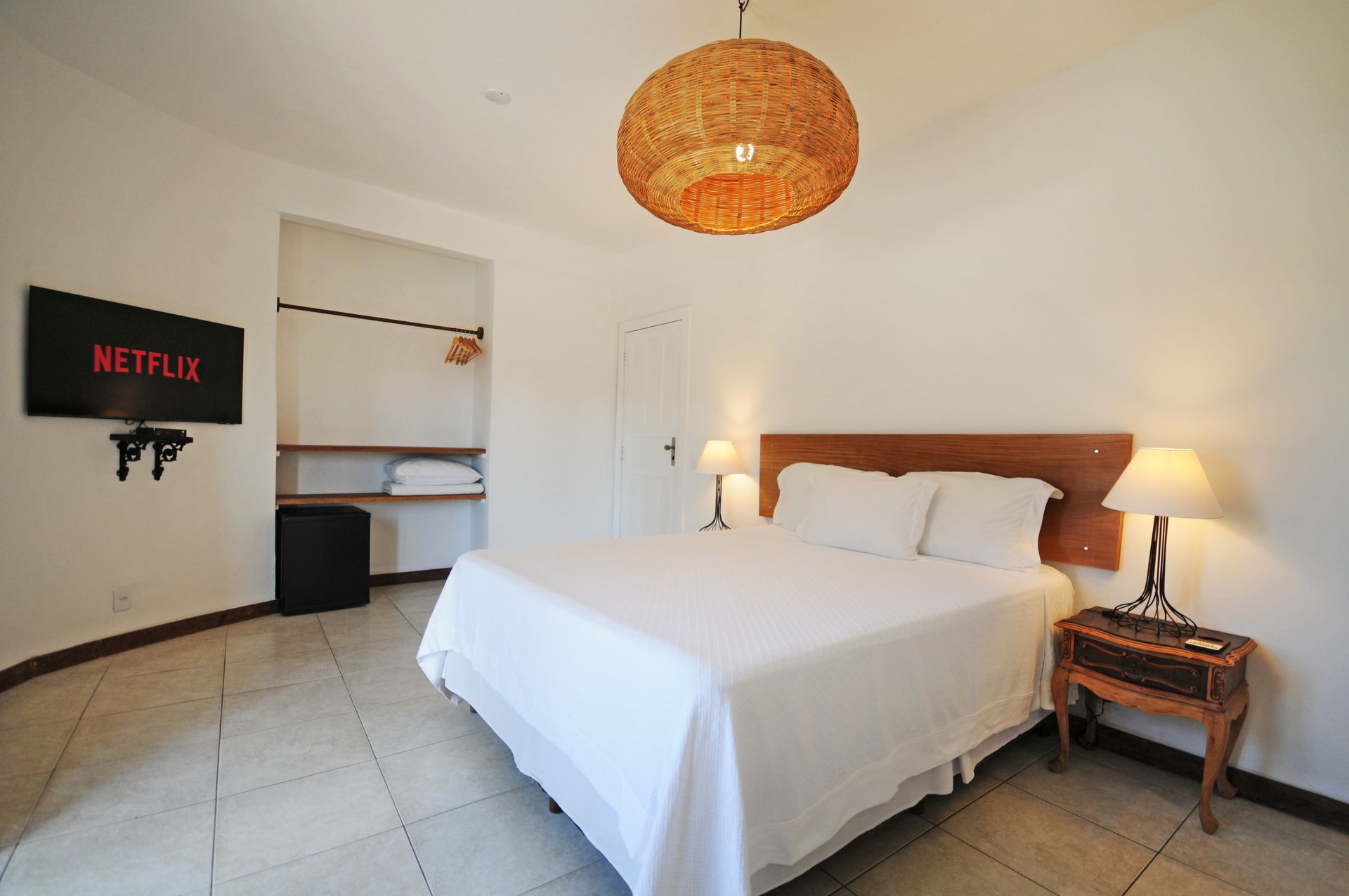 Bedroom with a bed, TV, nightstand, and wicker light fixture. White walls and tiled floor.