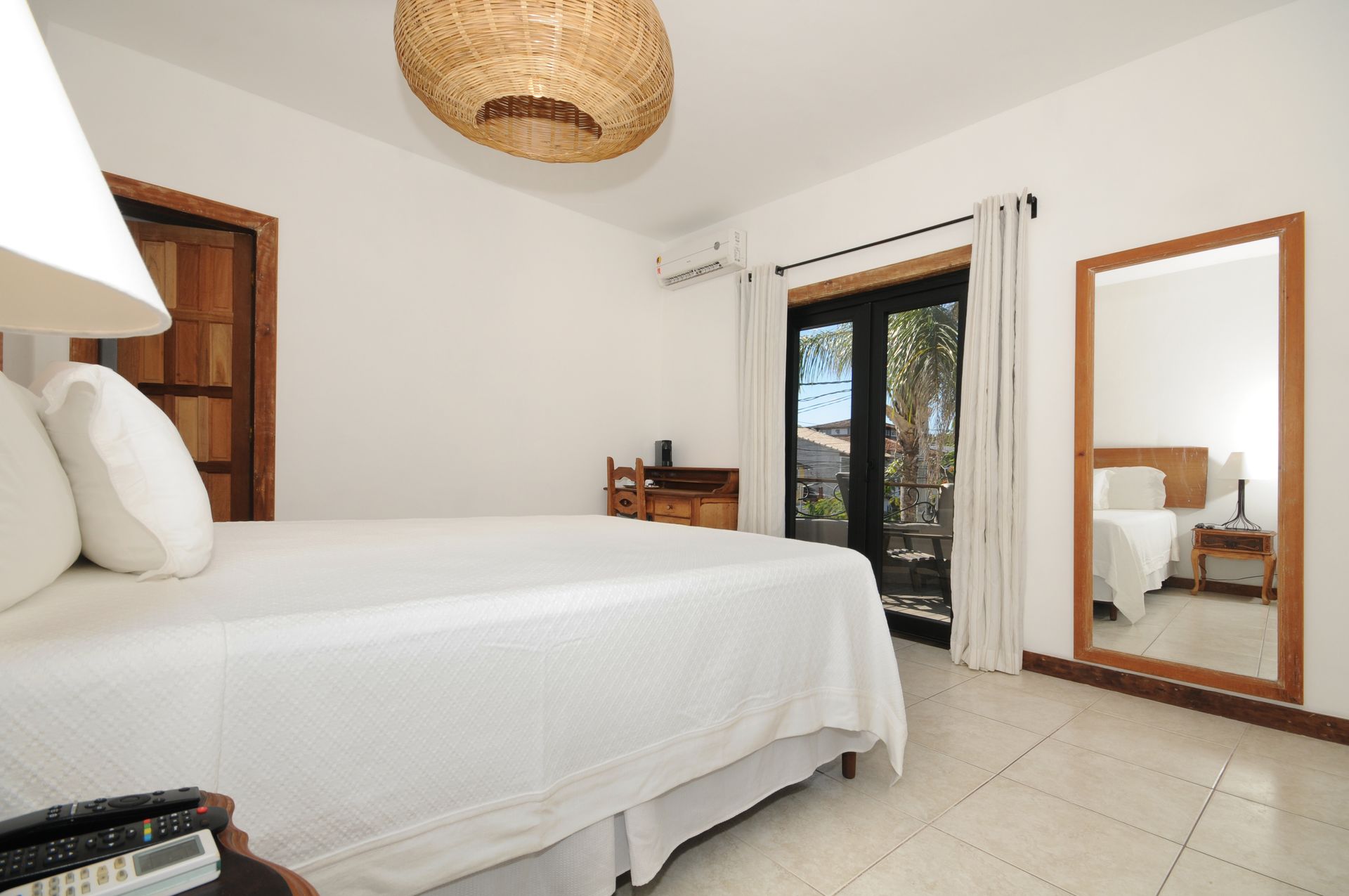 Bedroom with white walls, bed, wooden door/trim, large mirror, and open doors to outside view.