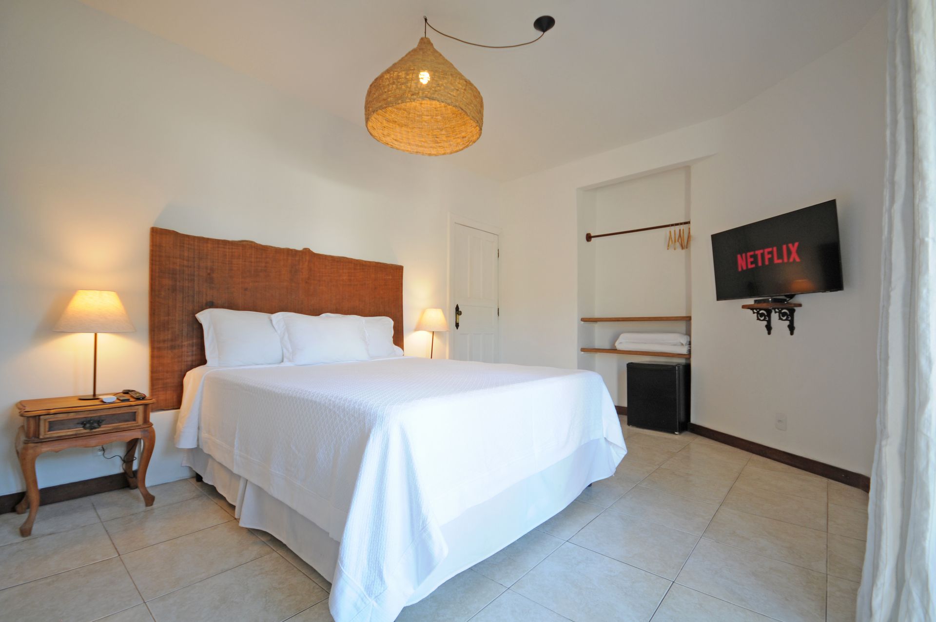 Bedroom with a white bed, woven headboard, lamp, TV, and woven pendant light.