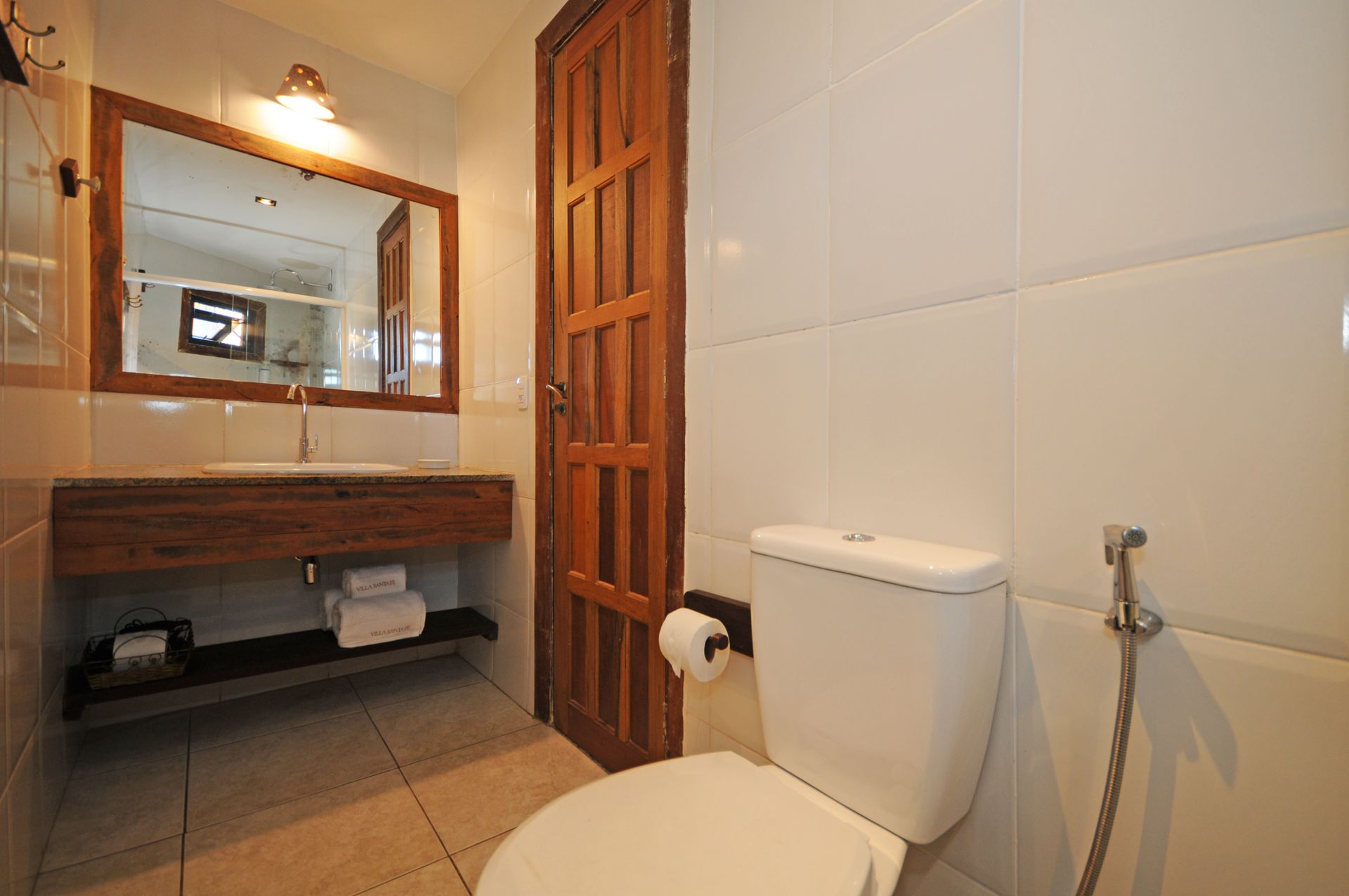 Bathroom with white walls, toilet, wooden door, sink, and mirror.
