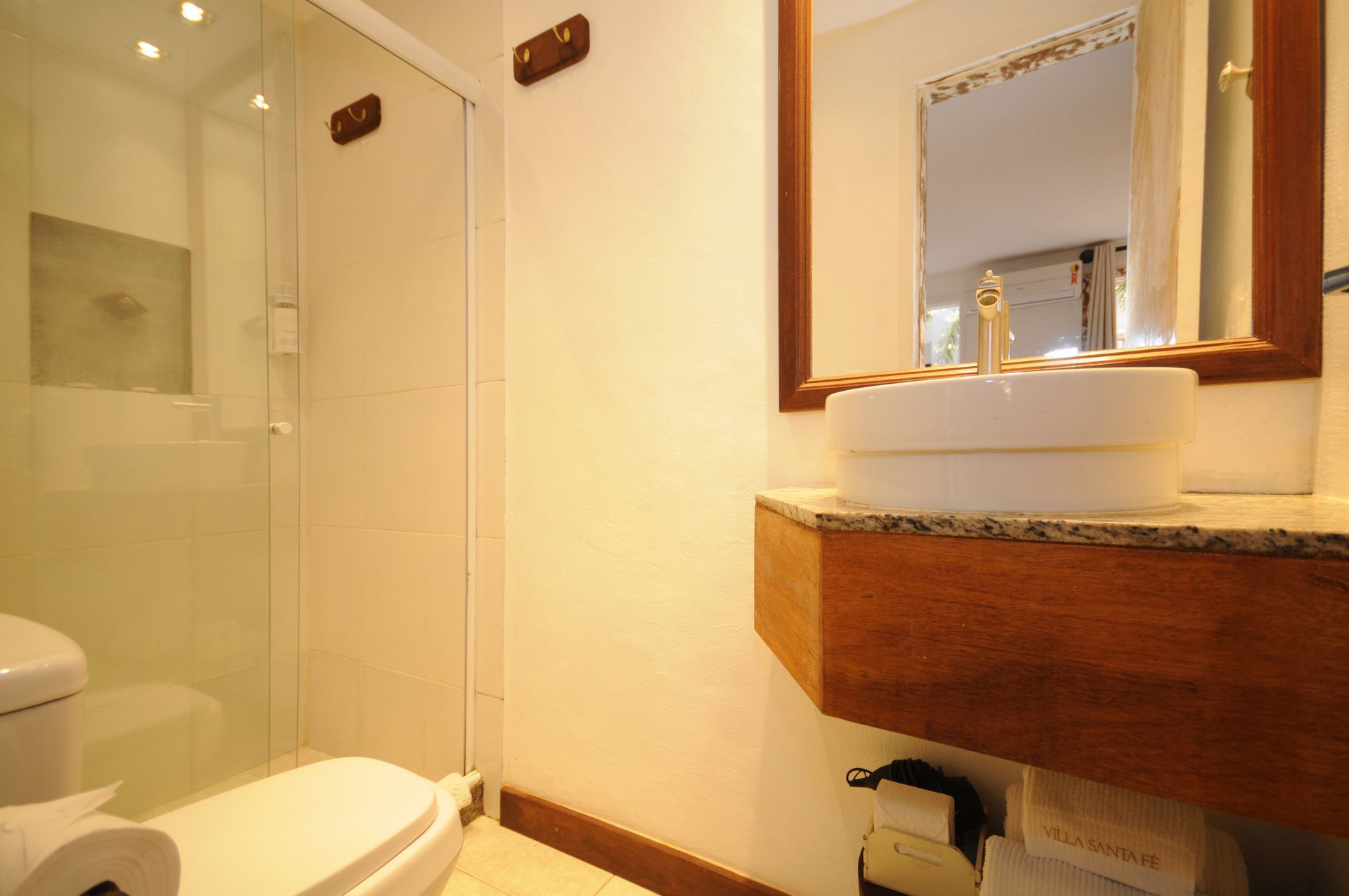 Bathroom with a glass shower, white toilet, a wooden cabinet, and a round sink with a mirror.