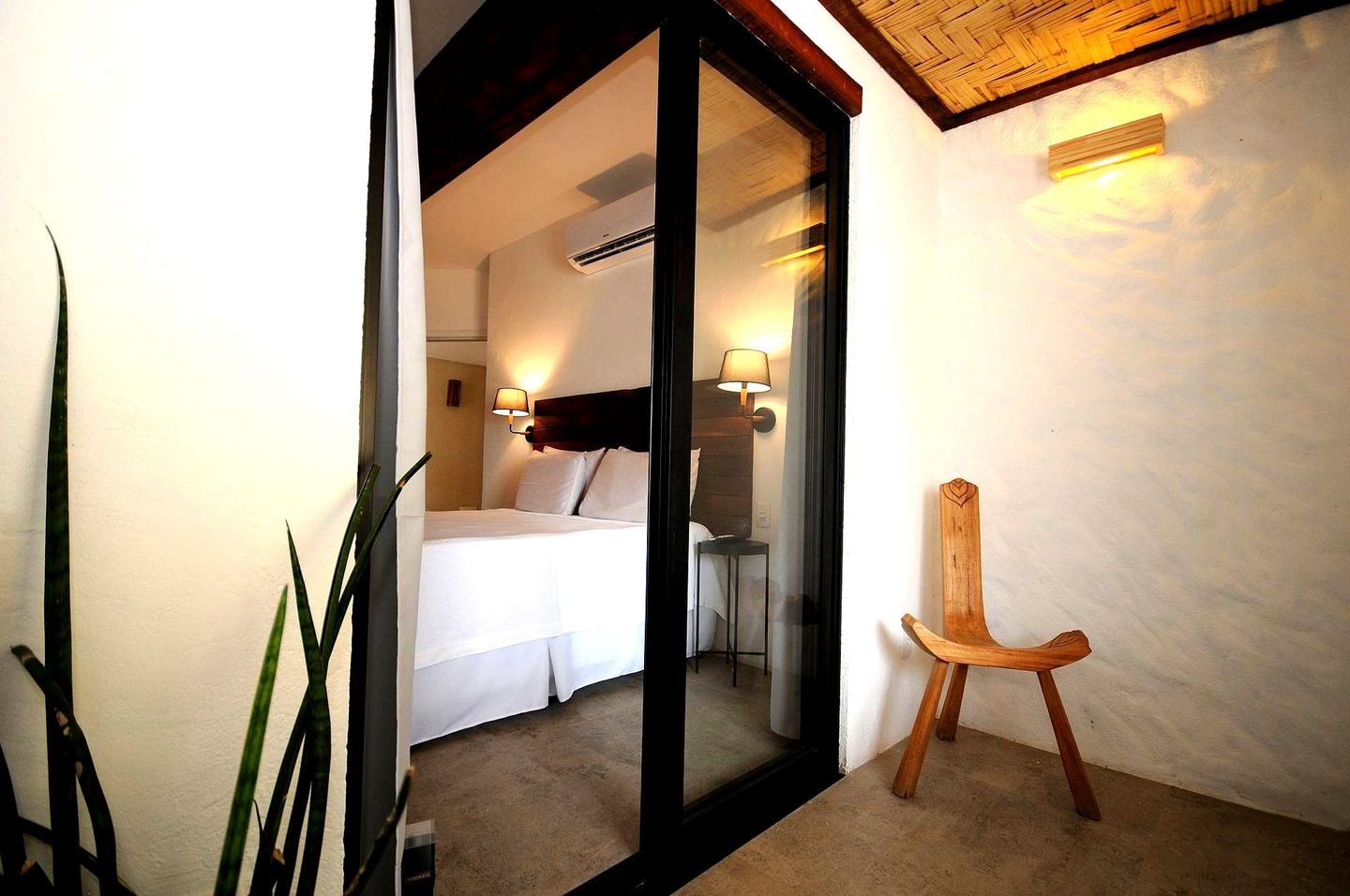 A doorway reveals a bright bedroom with a bed. A wooden chair sits outside, next to a textured wall.