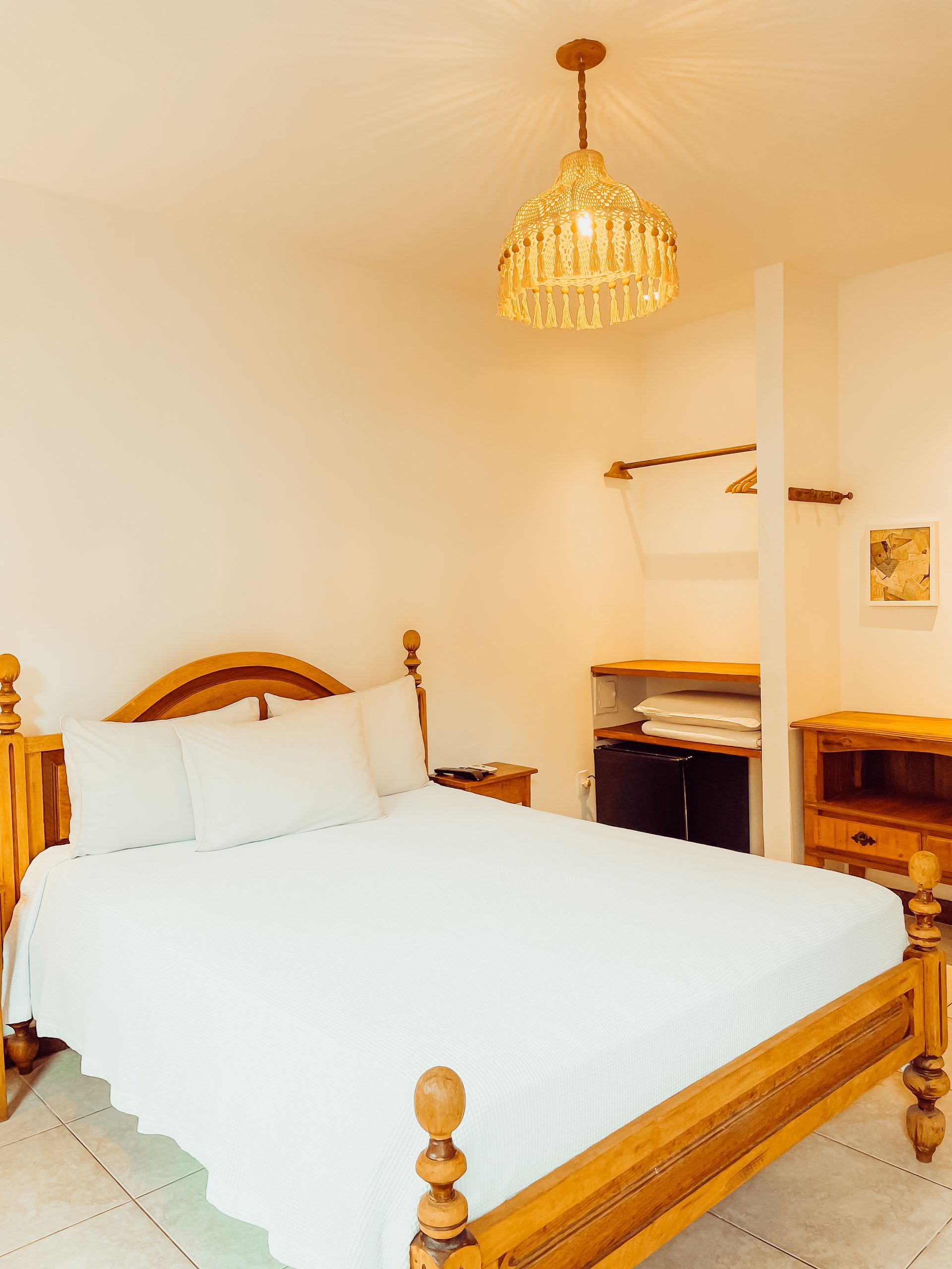 Bedroom with wooden furniture, including a bed, nightstand, and dresser. A decorative light hangs from the ceiling.