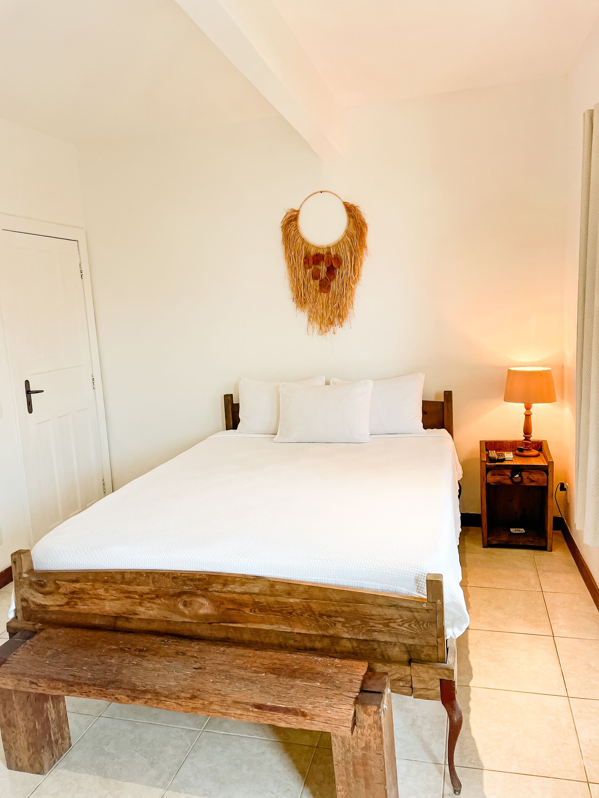 Bedroom with wooden bed frame, bench, and nightstand. Decorative wall hanging above bed.