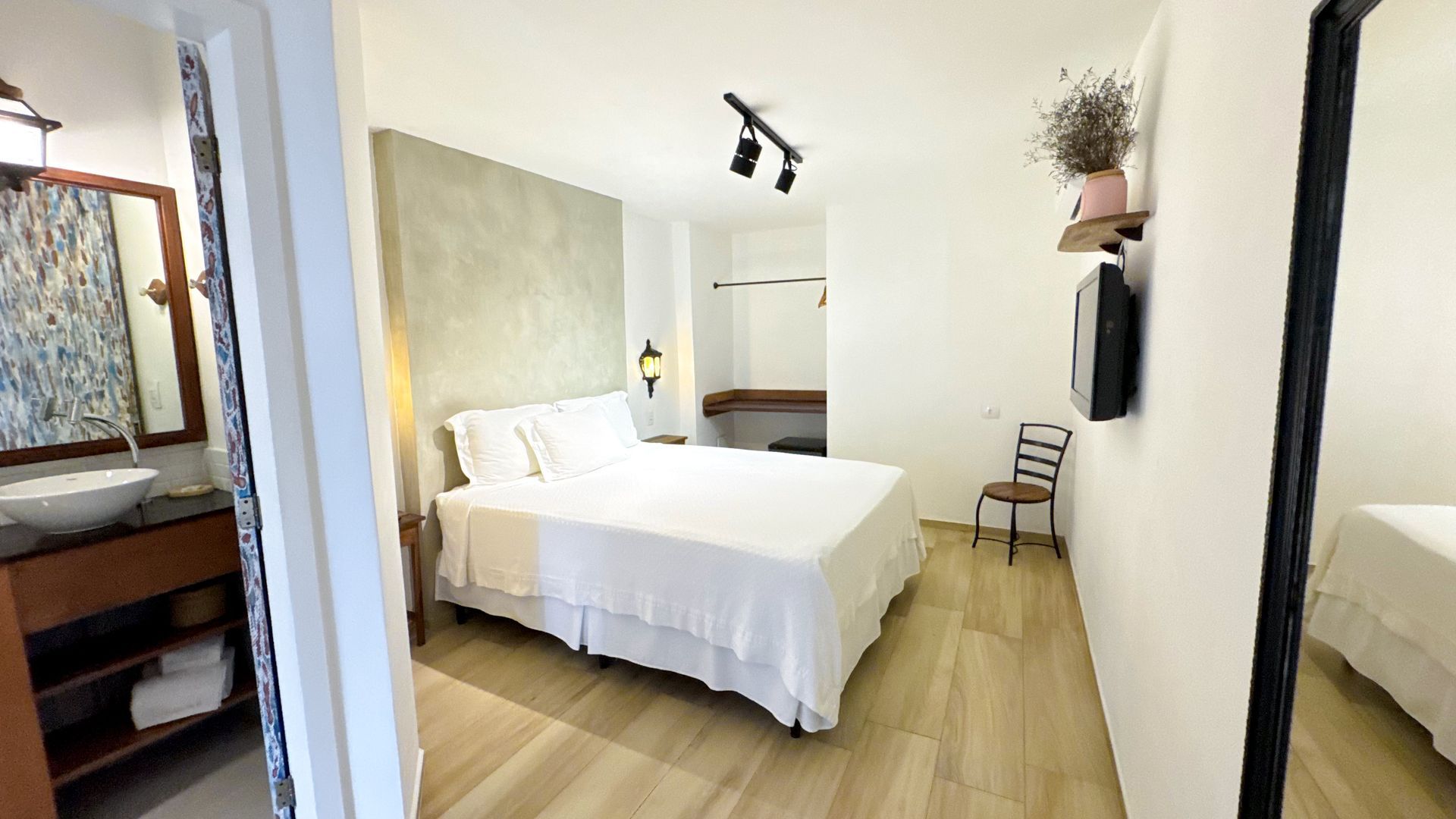 Bedroom with a double bed, bathroom on the left, and a small chair. White and light wood color scheme.