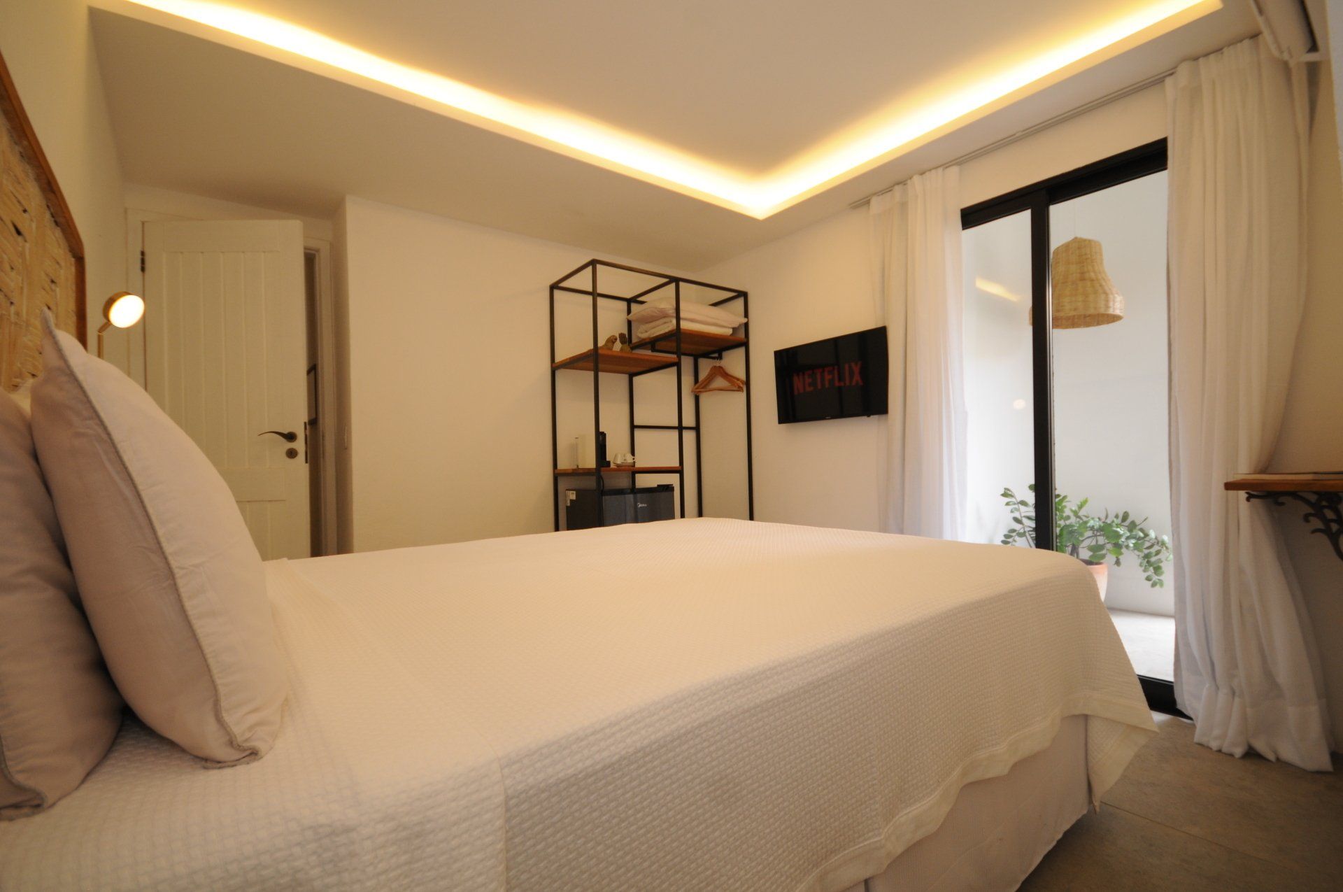 Bedroom with a large bed, open door to a balcony, shelving unit, and television.