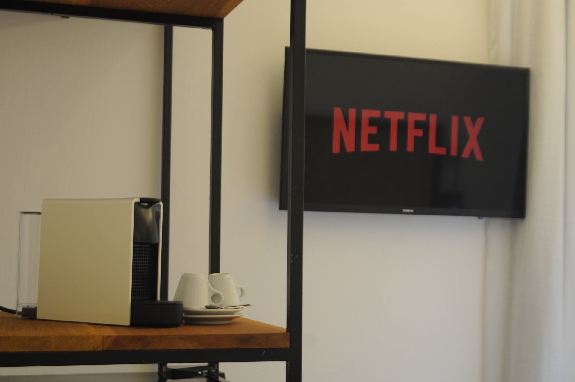 A television with the Netflix logo is mounted on a white wall above a coffee station.