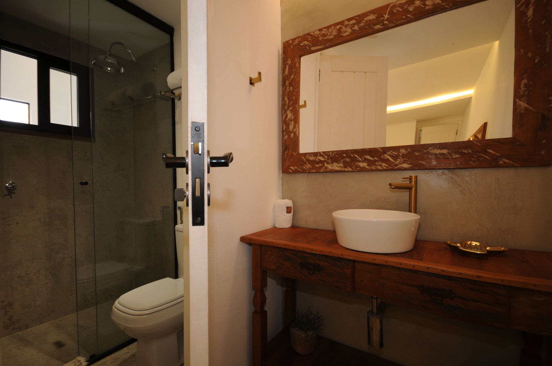 Bathroom with wooden vanity, round sink, large mirror, and glass-enclosed shower.