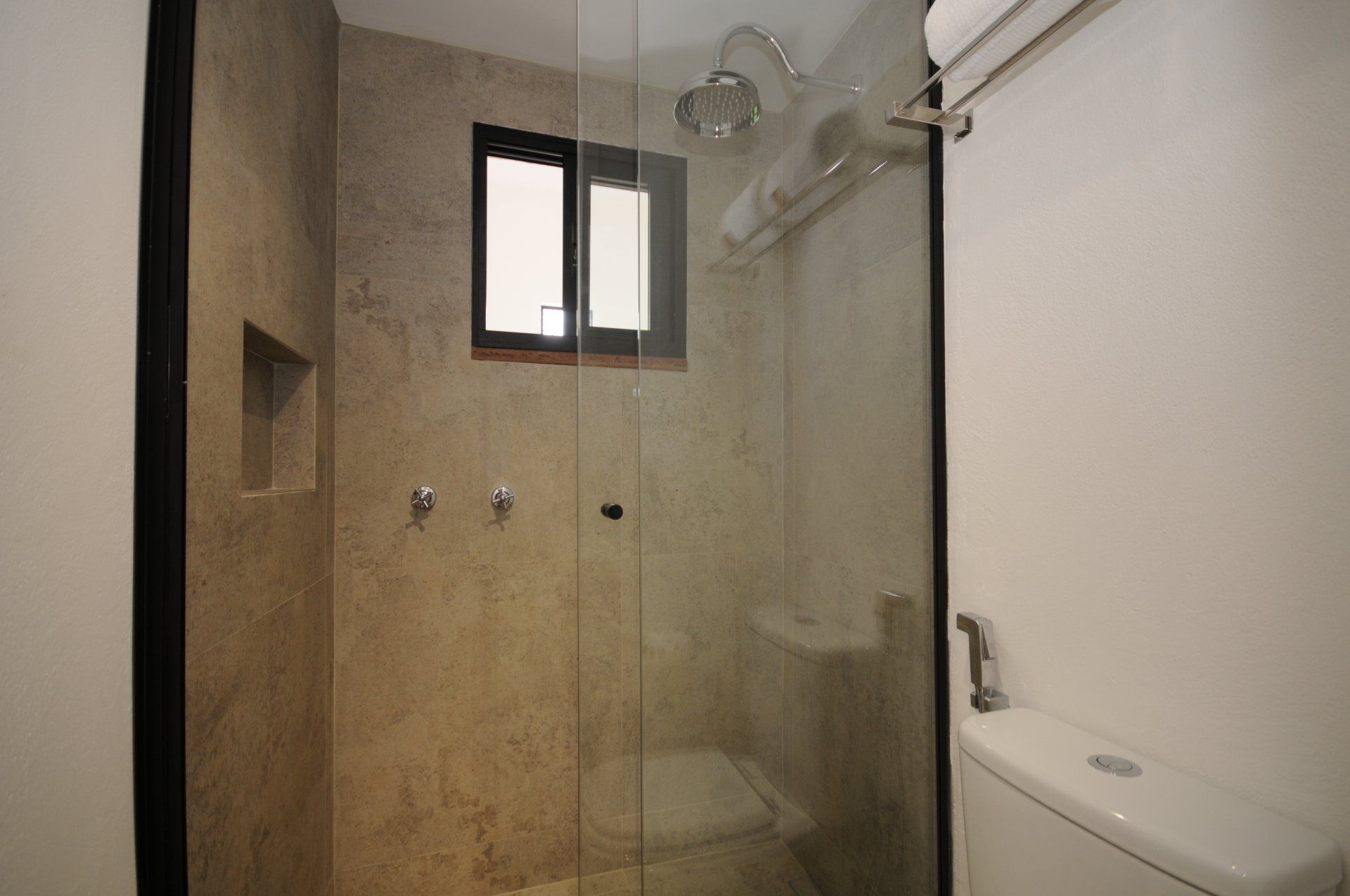 Shower stall with glass door, small window, and wall-mounted shower head and fixtures.