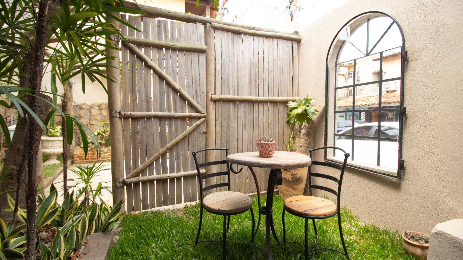 Small courtyard with a table, chairs, wooden gate, and arched window.