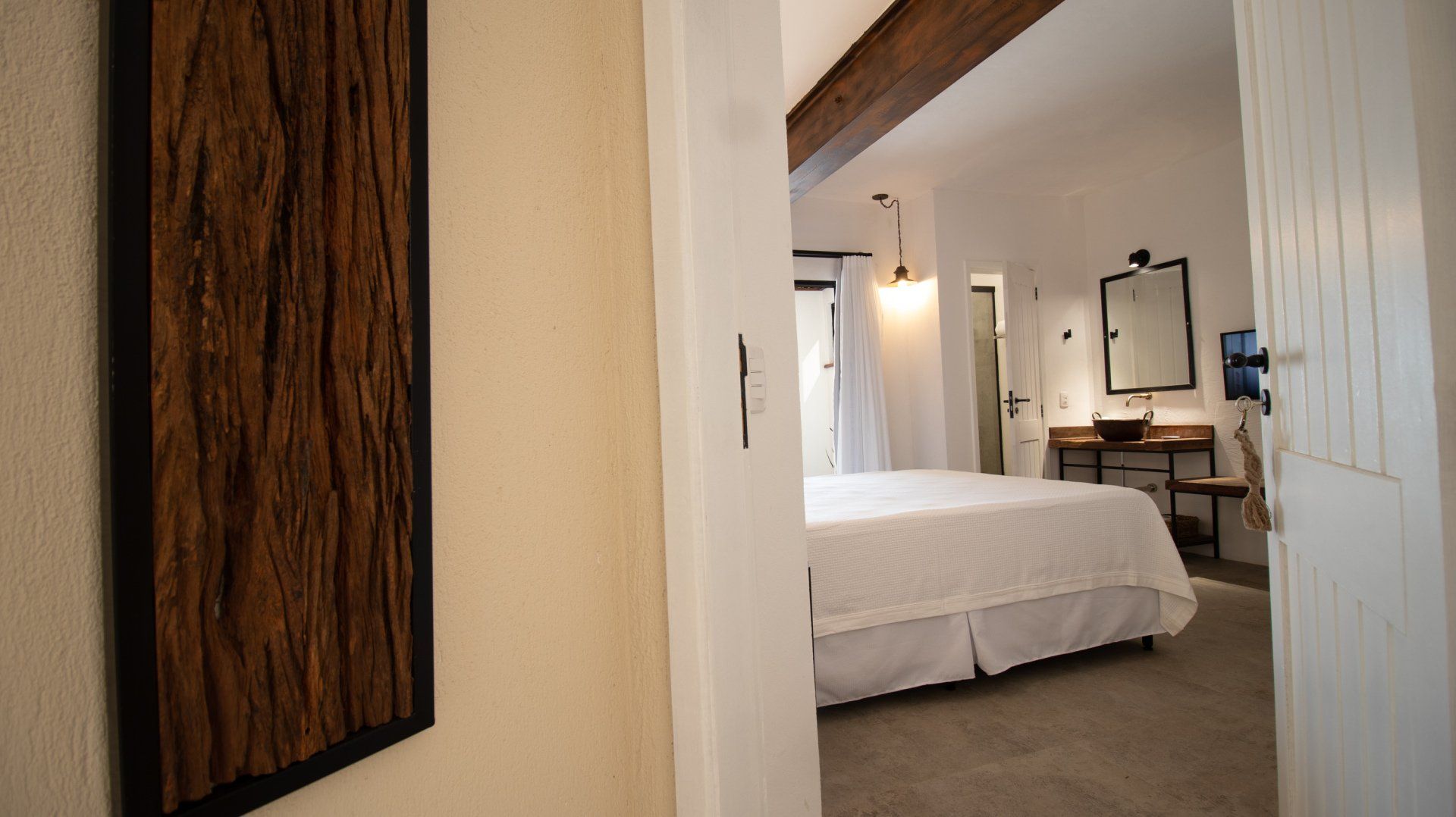 View of a bright bedroom from a doorway, featuring a bed, desk, and rustic artwork on the wall.