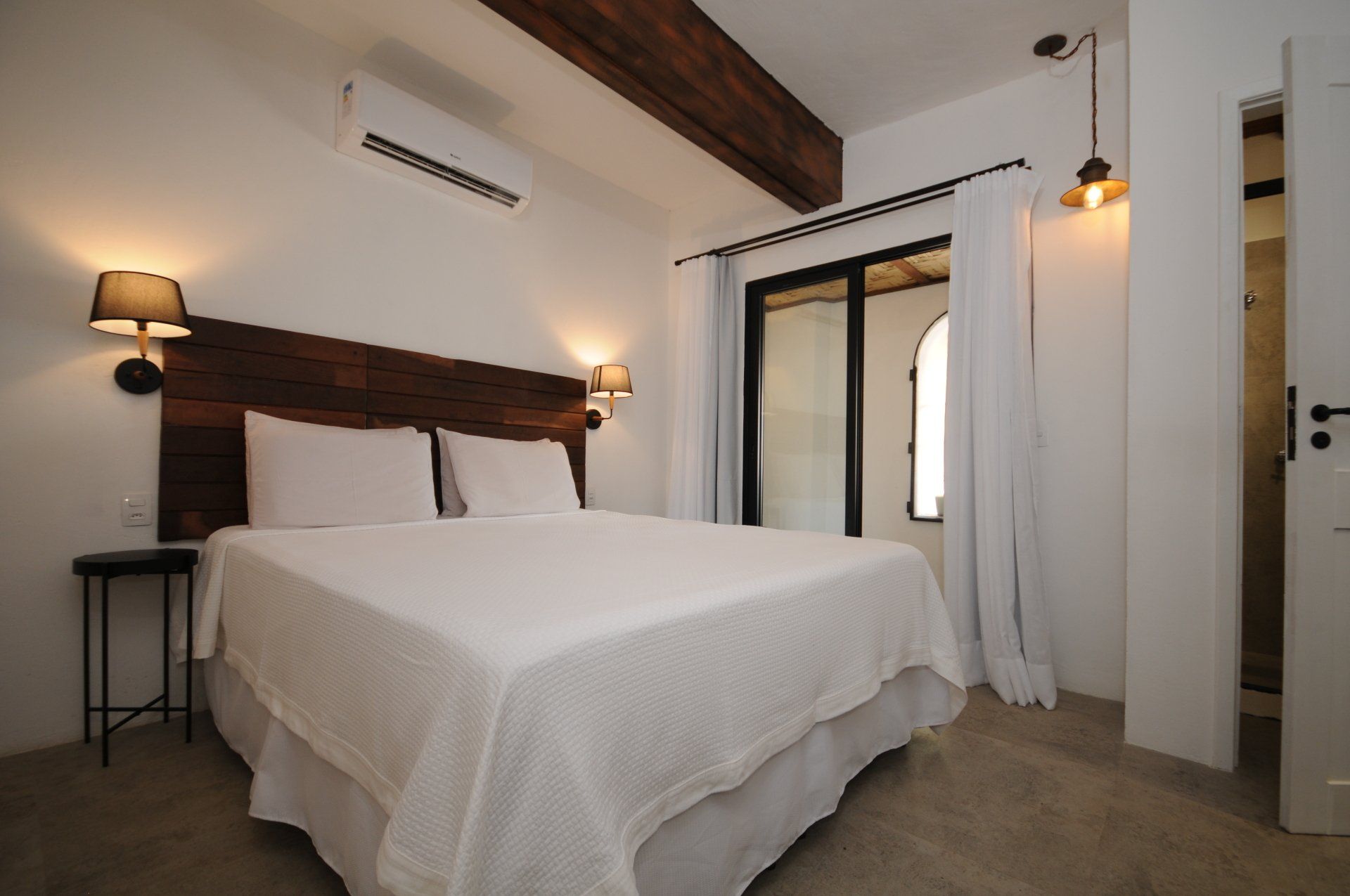 Bedroom with white bed, wooden headboard, and balcony access.  Beams and neutral color palette.