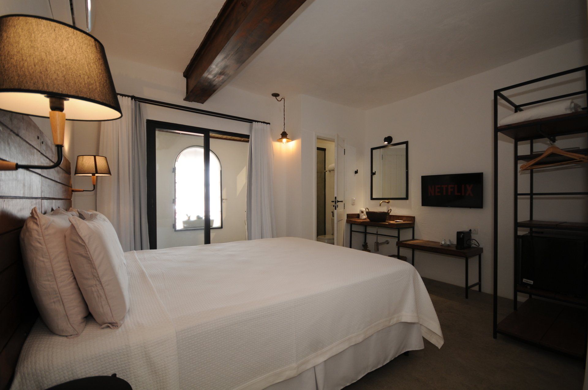 Bedroom with a large bed, balcony, wooden beams, and a Netflix-enabled TV.