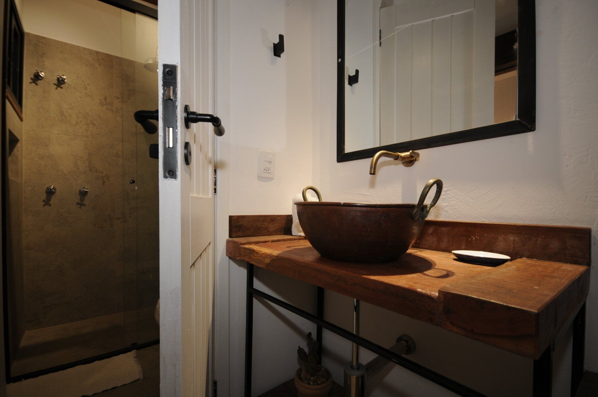Bathroom with a rustic wooden countertop, copper sink, and a shower with concrete walls.