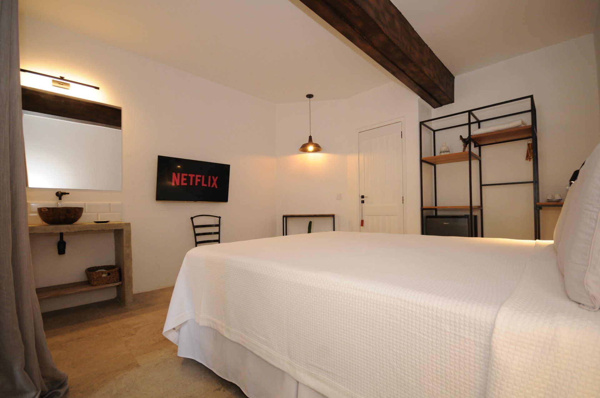 Bedroom with white bed, Netflix on TV, wooden beam and shelving unit.