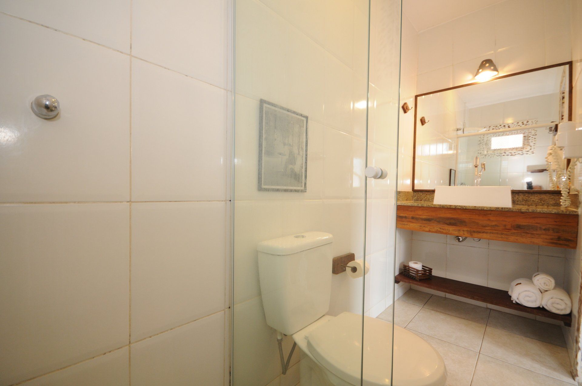 Bathroom interior with white tiled walls, toilet, glass shower door, and vanity with mirror.