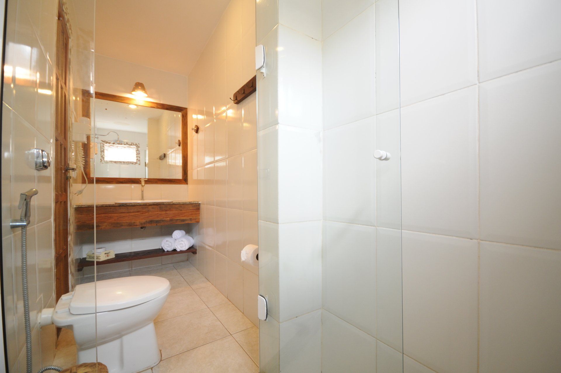 Bathroom with white tiled walls, glass shower, wooden vanity, and a toilet.