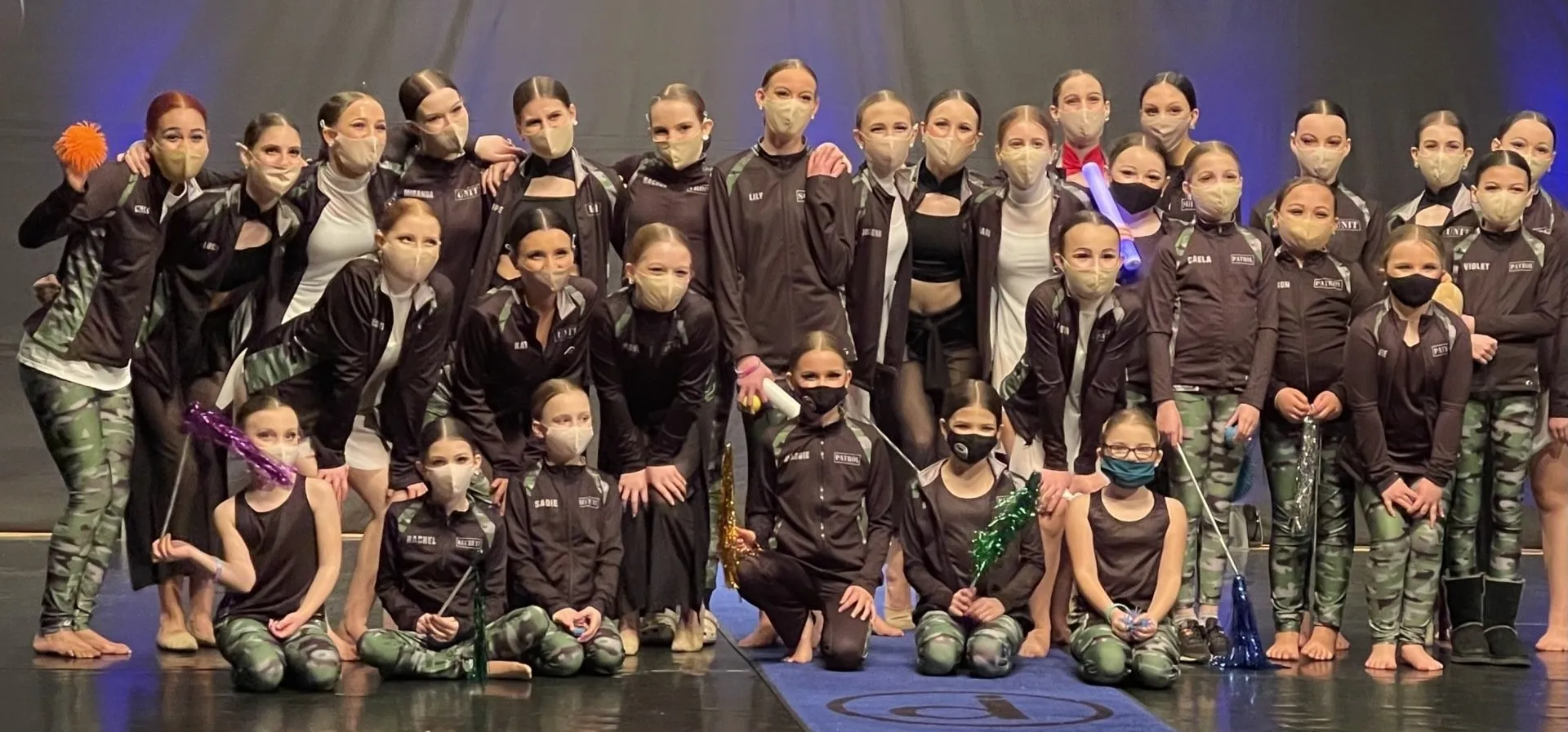 A group of young girls wearing face masks are posing for a picture on a stage.