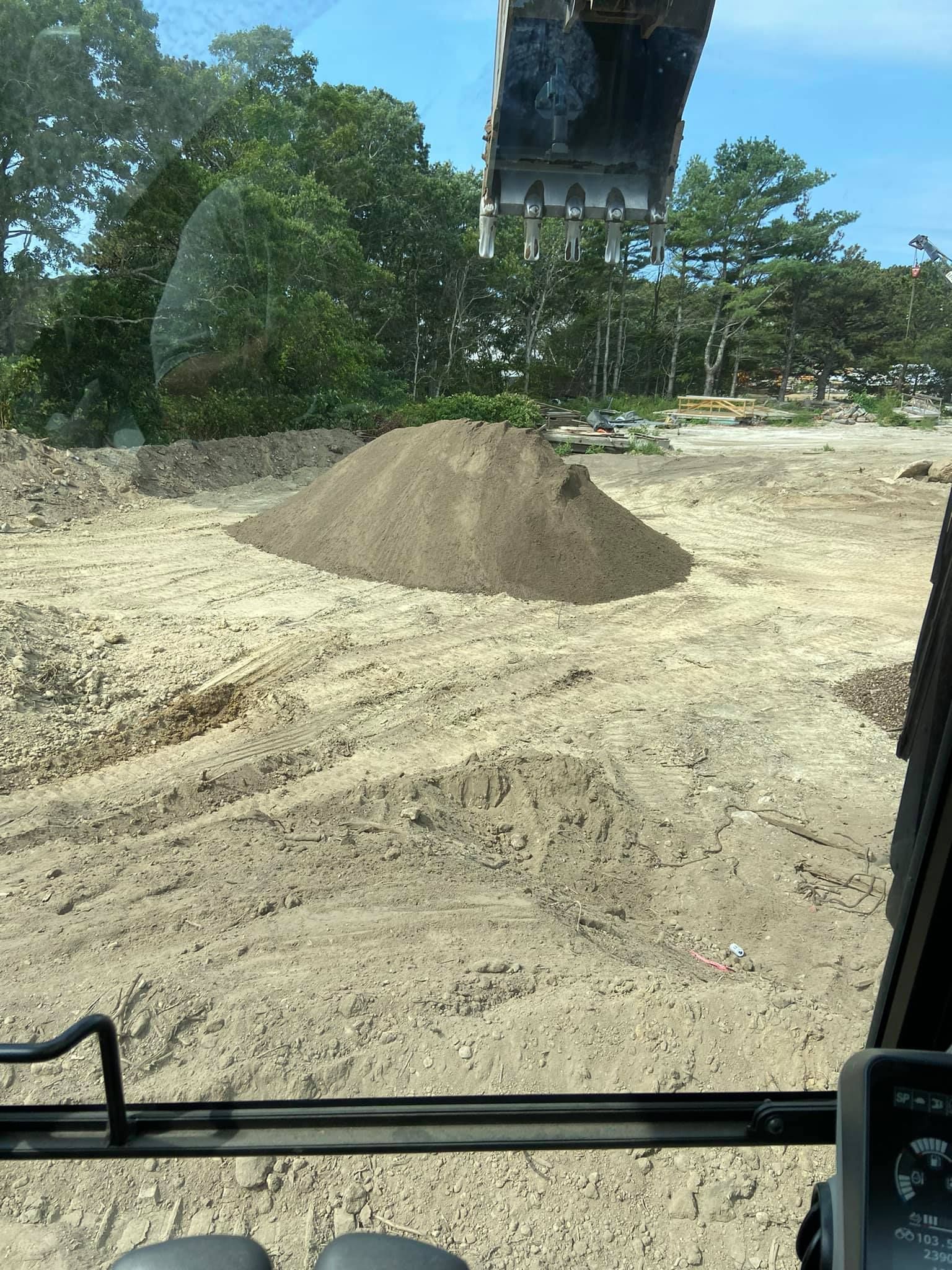 A pile of dirt on a construction site, viewed from inside heavy machinery. Trees in the background.