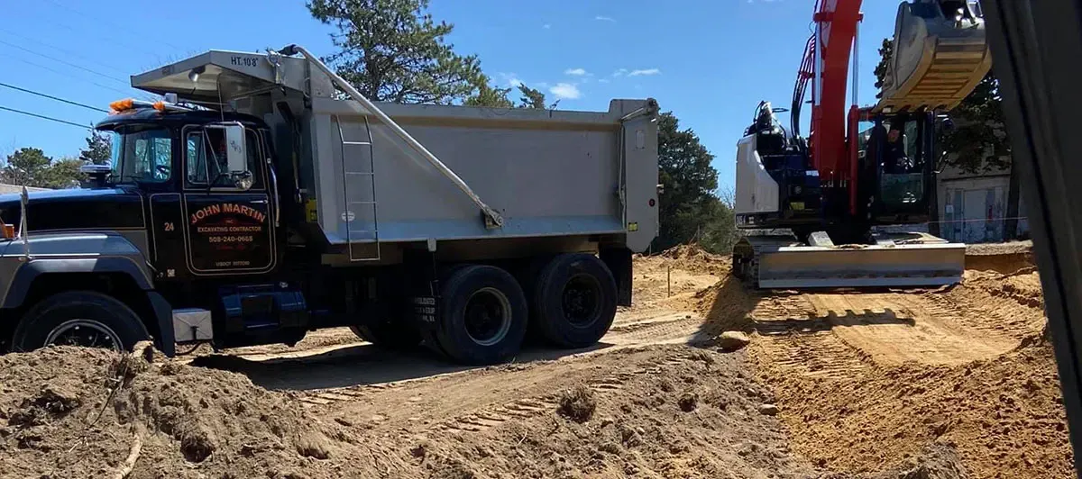 An excavator loading a dump truck with dirt on a construction site; sunny day.