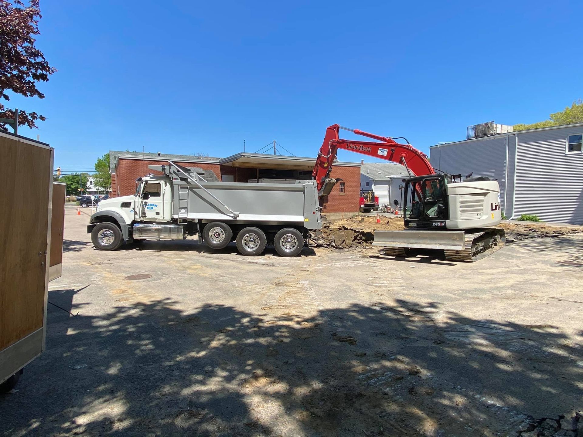An excavator loading a white dump truck with dirt on a construction site under a blue sky.