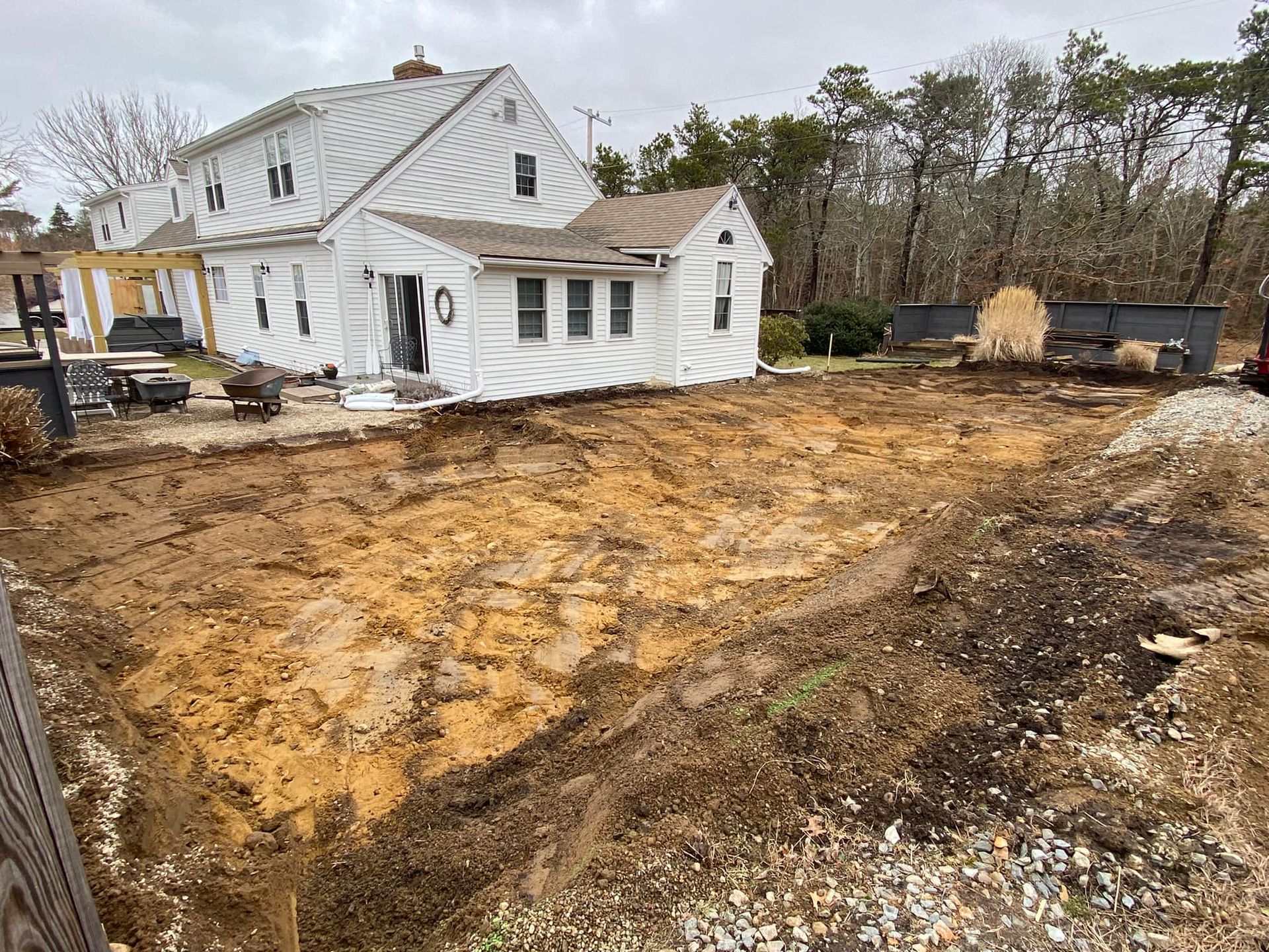 House undergoing renovation; excavation in front. Building wrapped in white material, surrounded by dirt and debris.