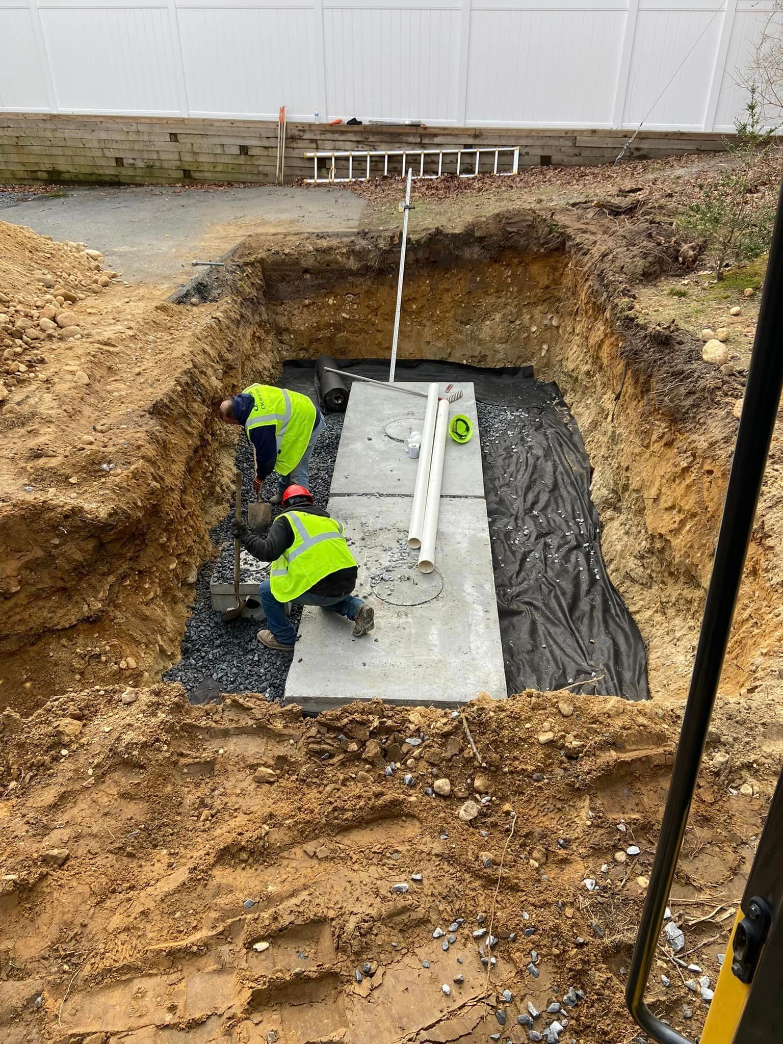 Construction workers in neon vests installing a concrete structure in an excavated pit.