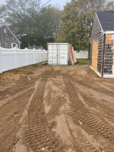 Muddy construction site with a white fence, shipping container, and partially built building.