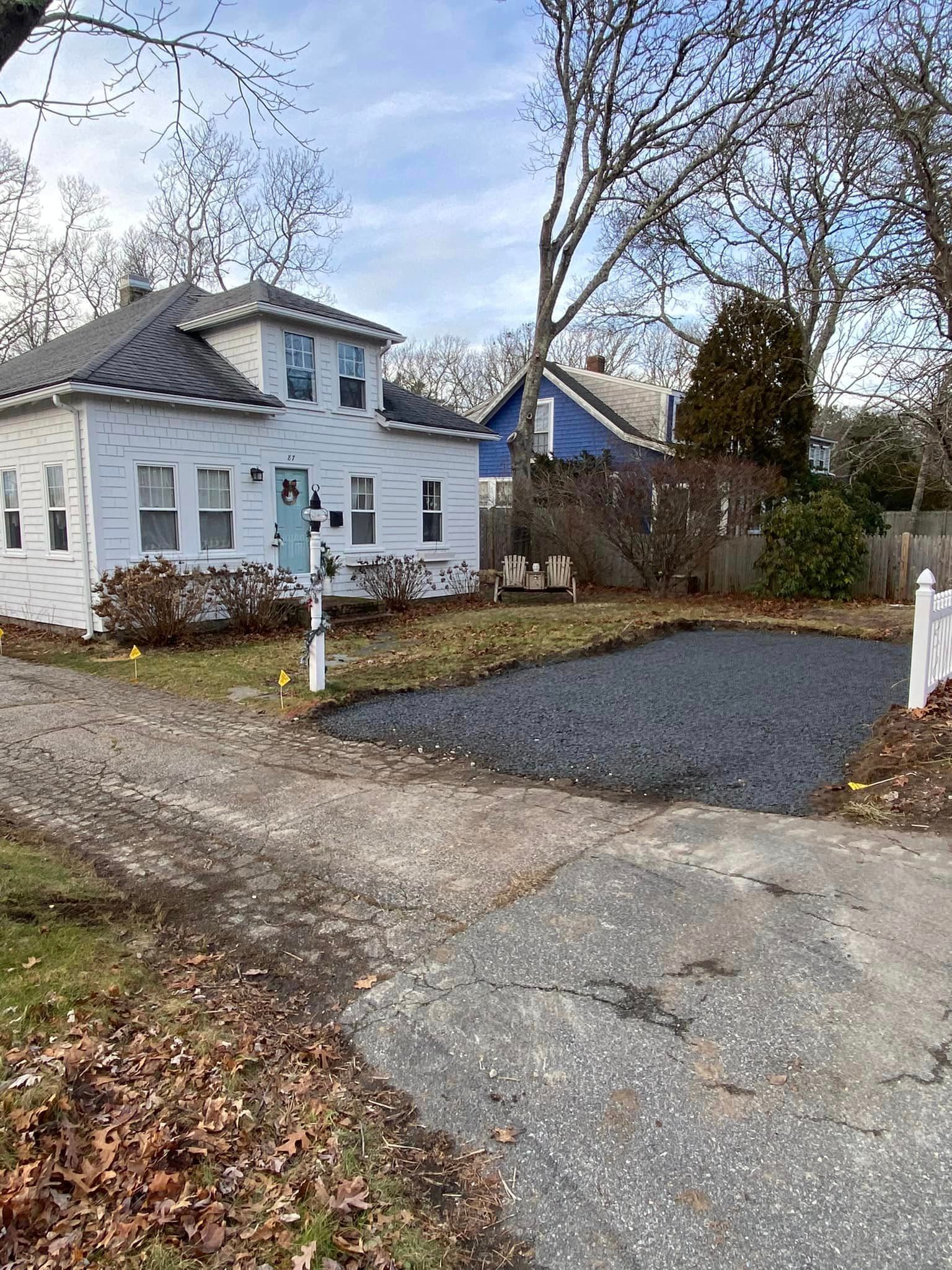 White house with a light blue door and gravel driveway; fallen leaves on the ground.