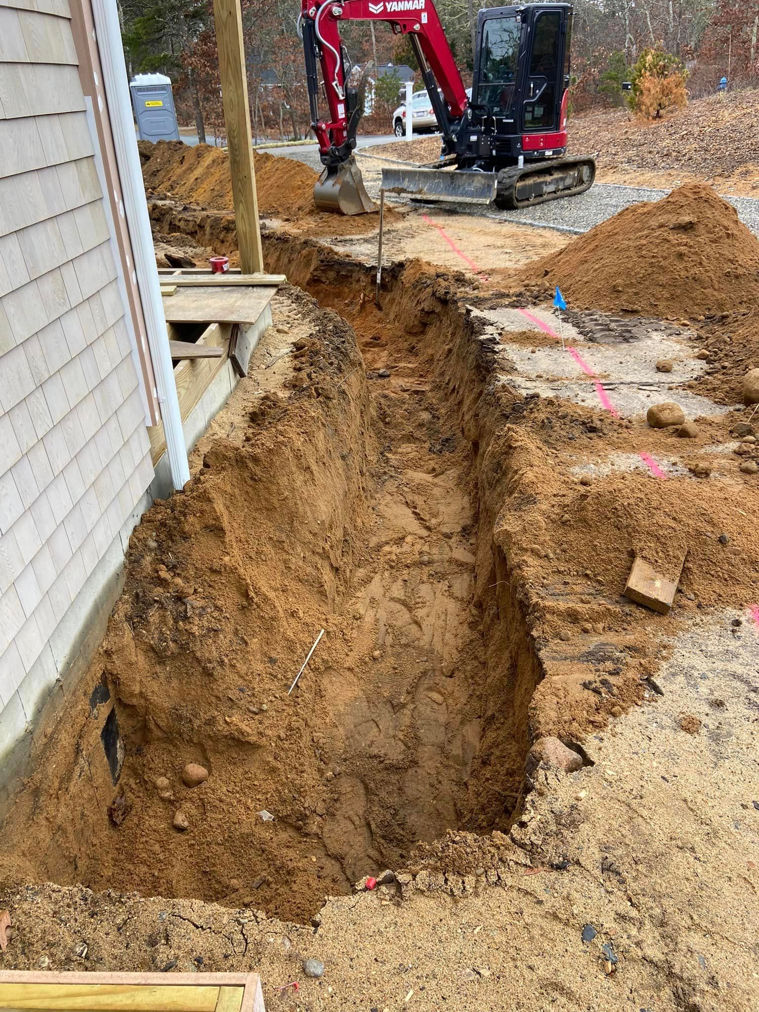 Excavation for construction beside a beige building. A small excavator sits in the background