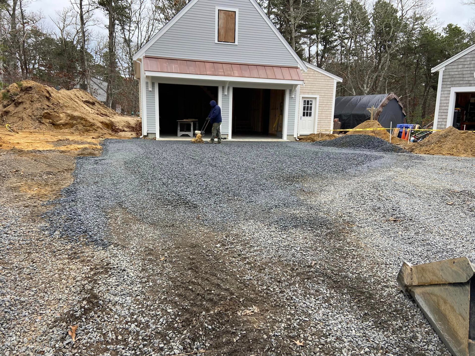 Gravel driveway leading to a two-car garage under construction; a person uses a machine inside.