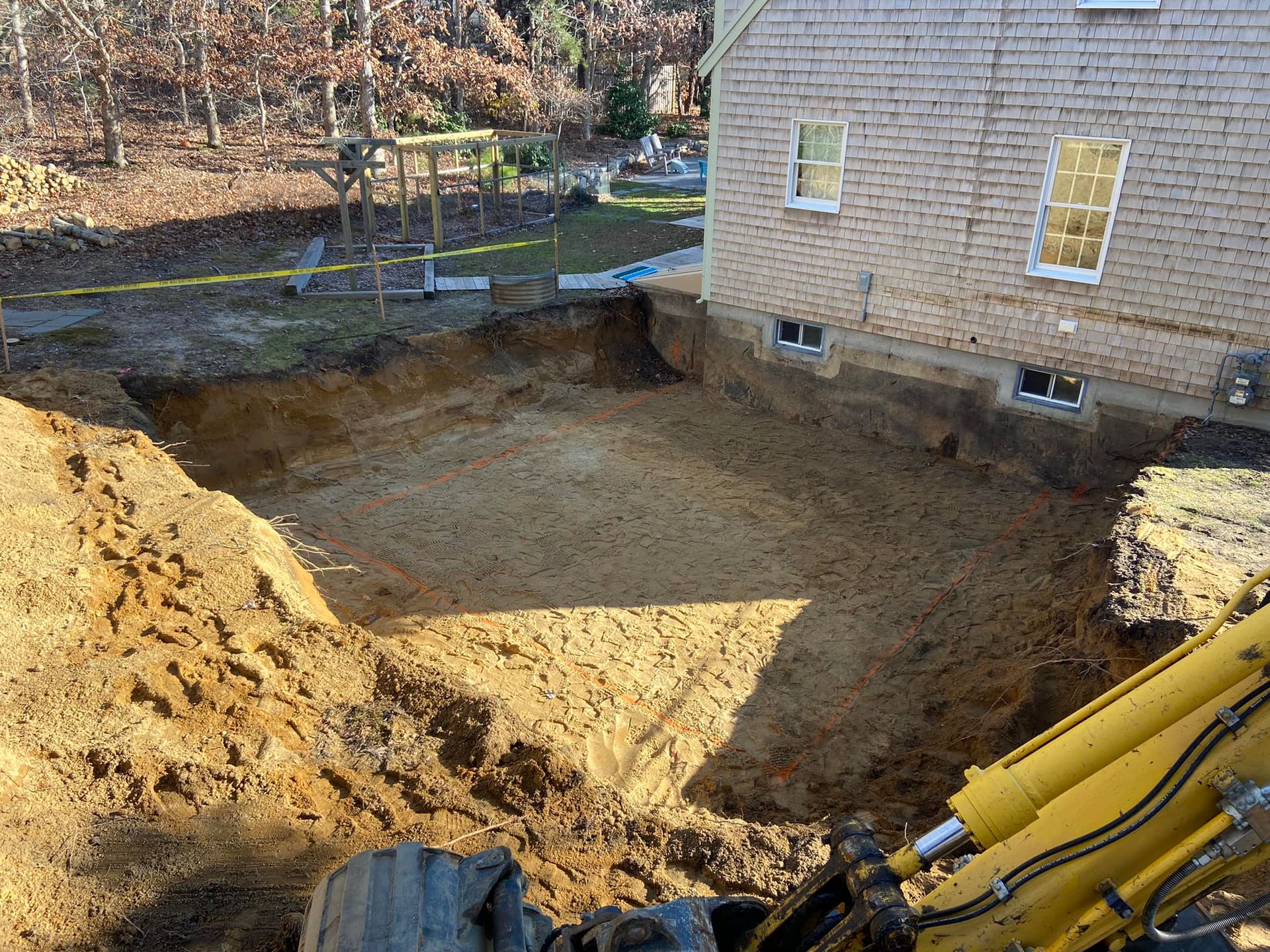 Excavated dirt pit next to a brick building; yellow construction equipment present. Sunlight.