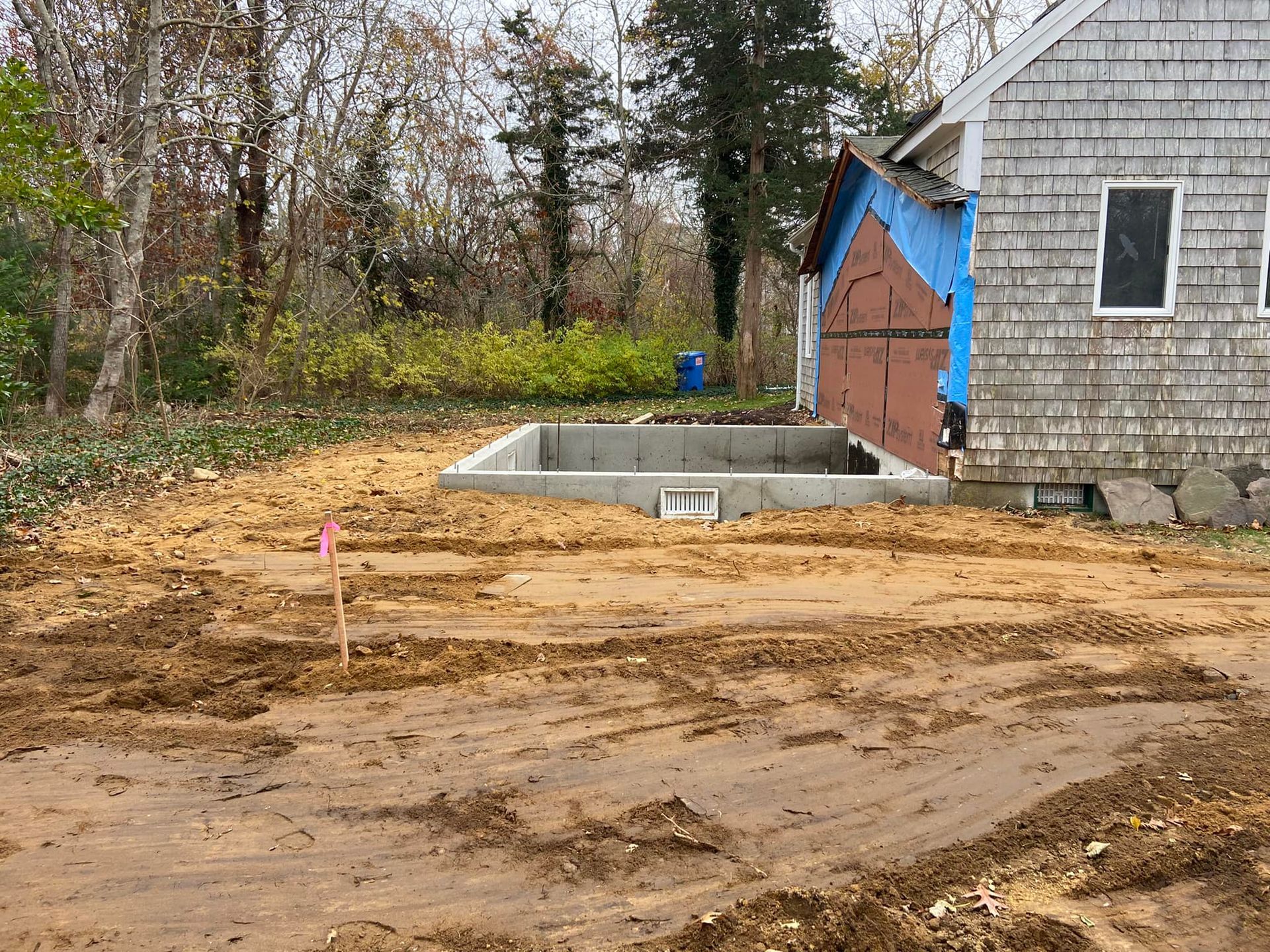 Dirt lot with concrete foundation next to a house with damaged siding.