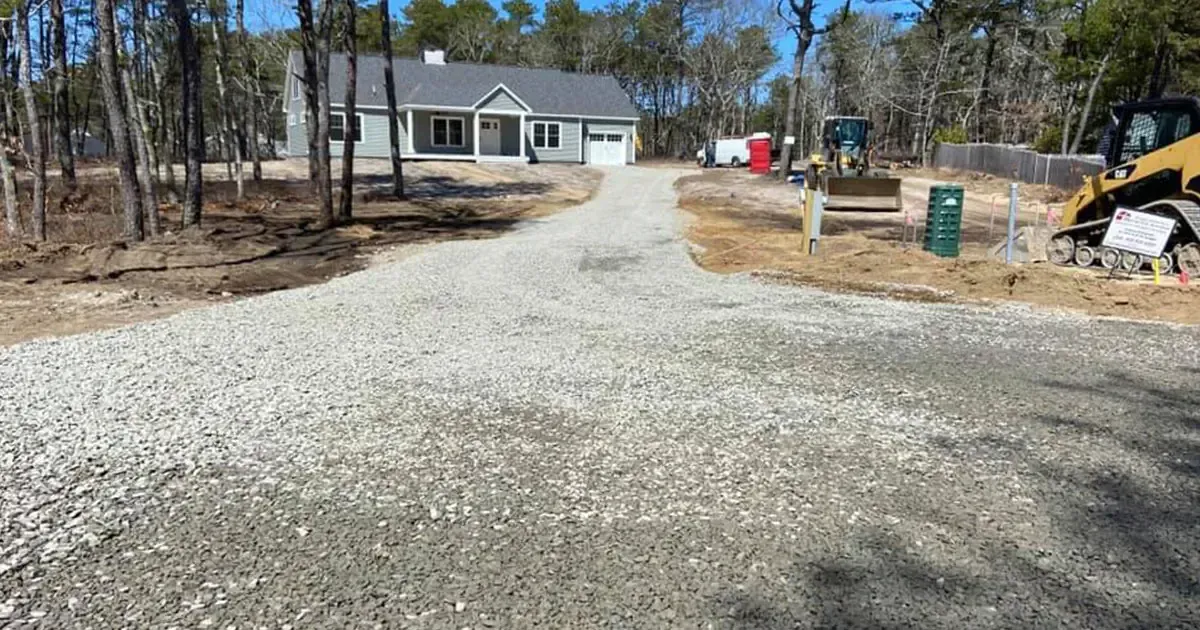 A gravel driveway leads to a house under construction; trees and construction equipment are visible.