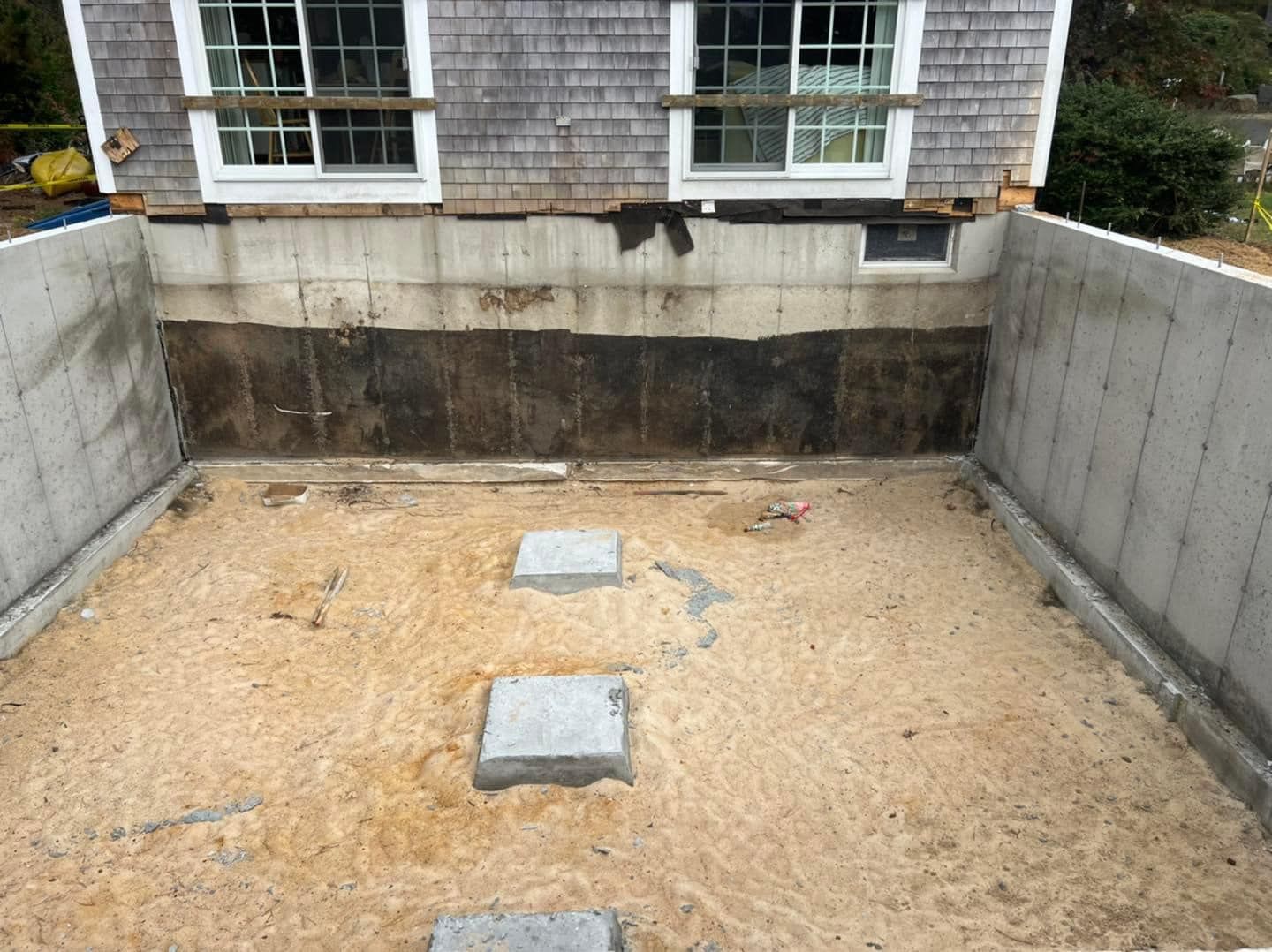 Basement under a house with concrete foundation walls, sand floor, and supports. Gray siding above.