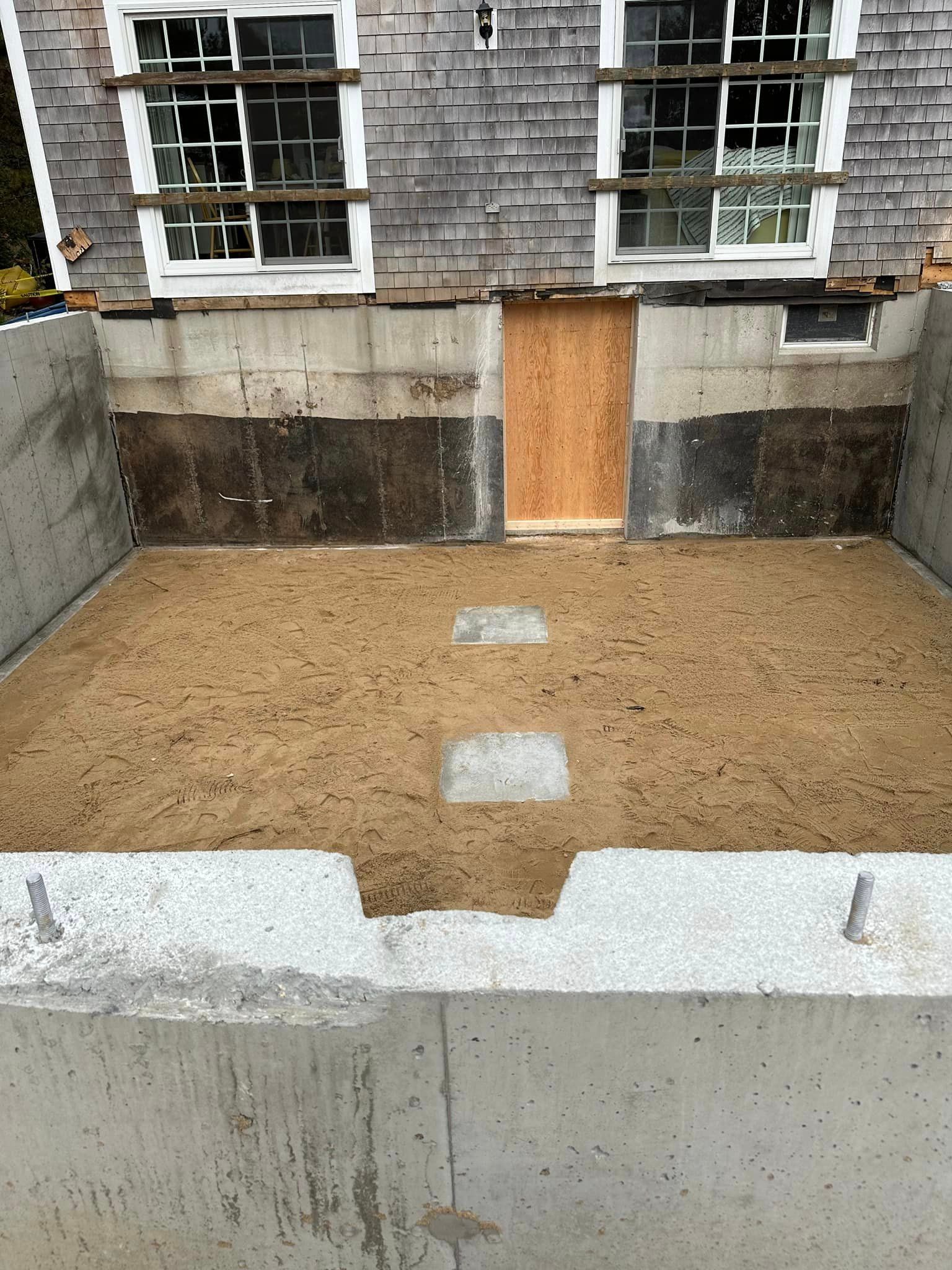Concrete foundation of a building with a sandy interior and a wooden door.