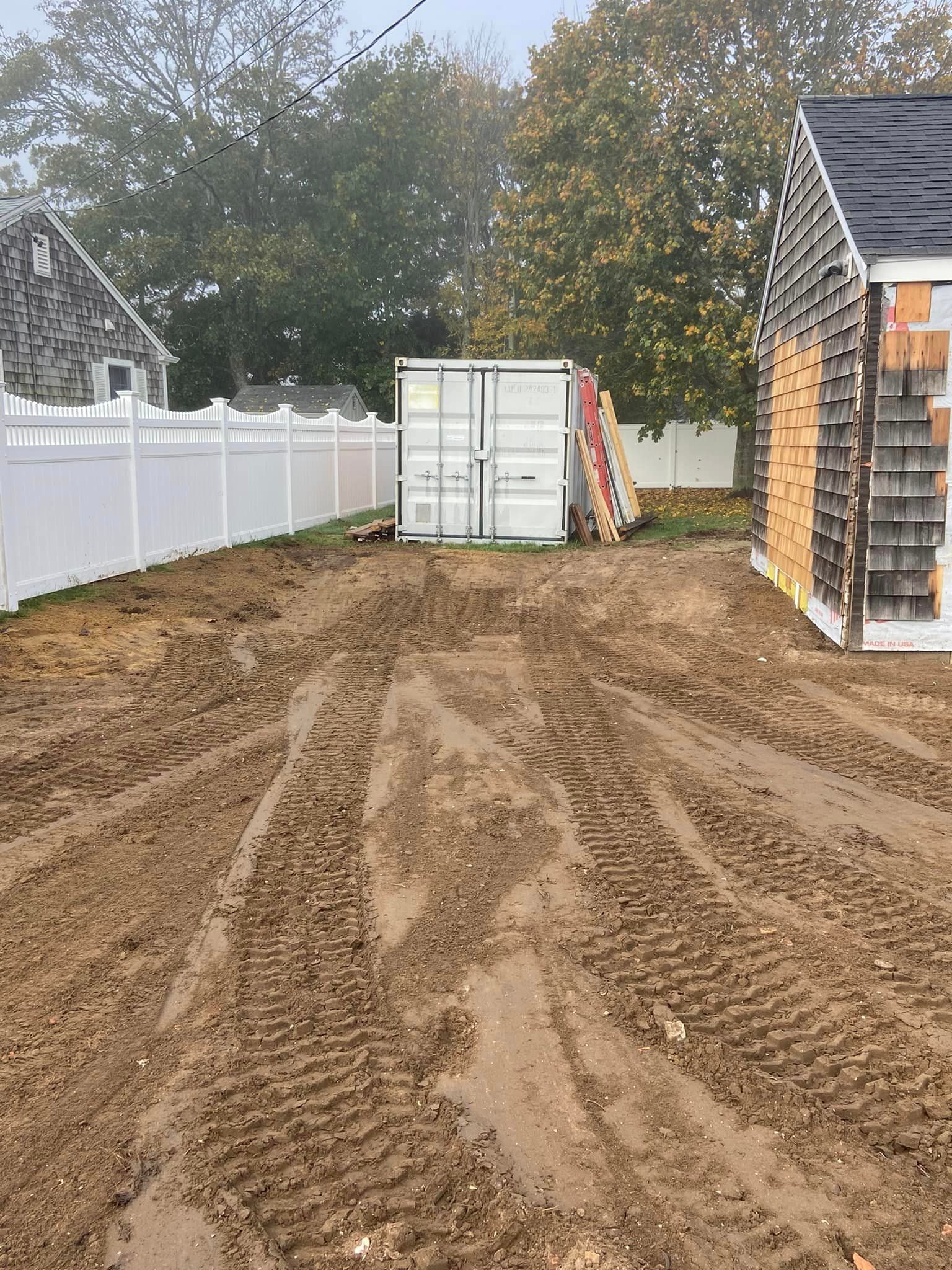 Muddy lot with tire tracks, white fence, storage container, and partially built shed.