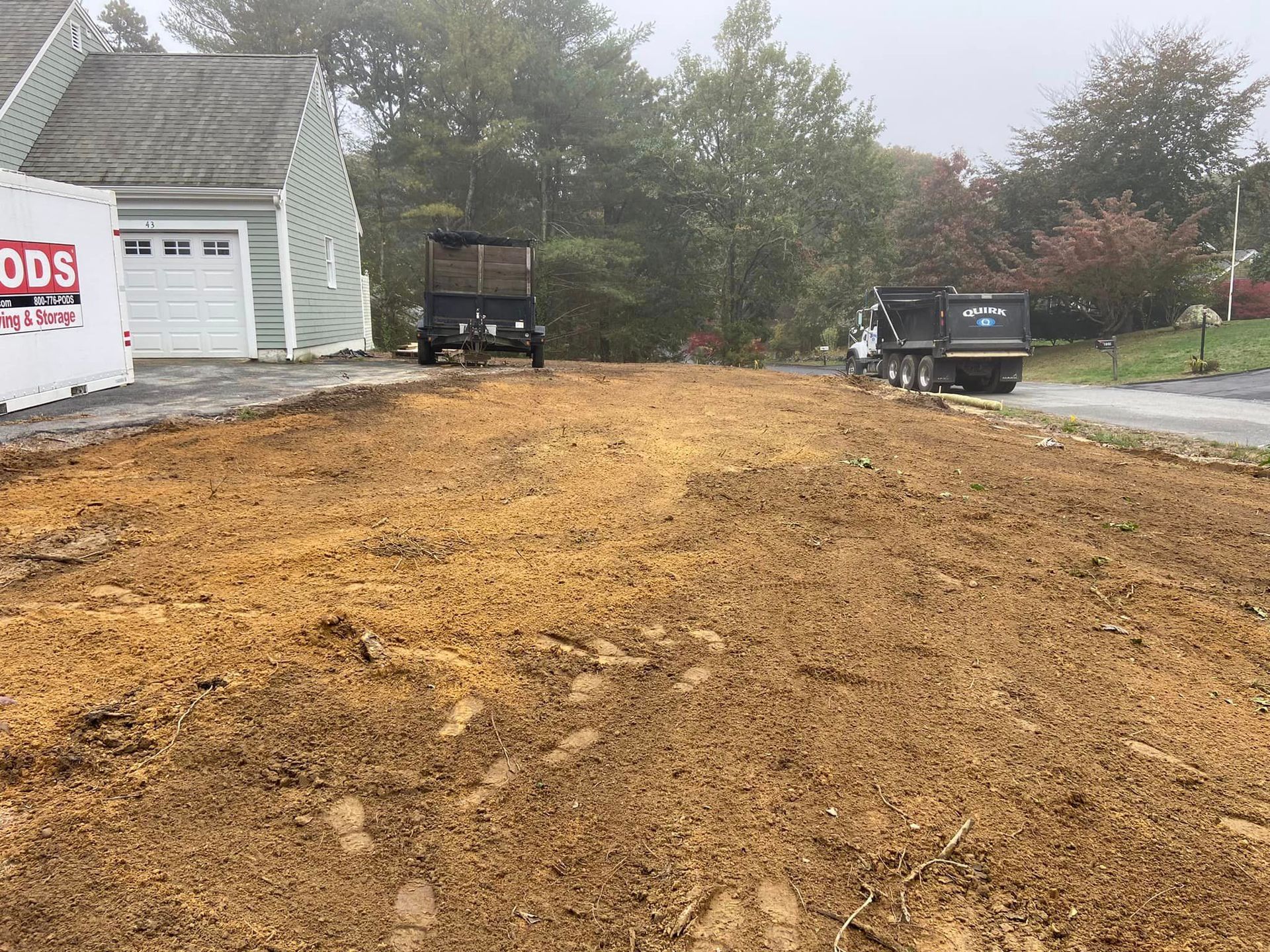 Dirt and gravel driveway with a house and vehicles in the background. Construction site.