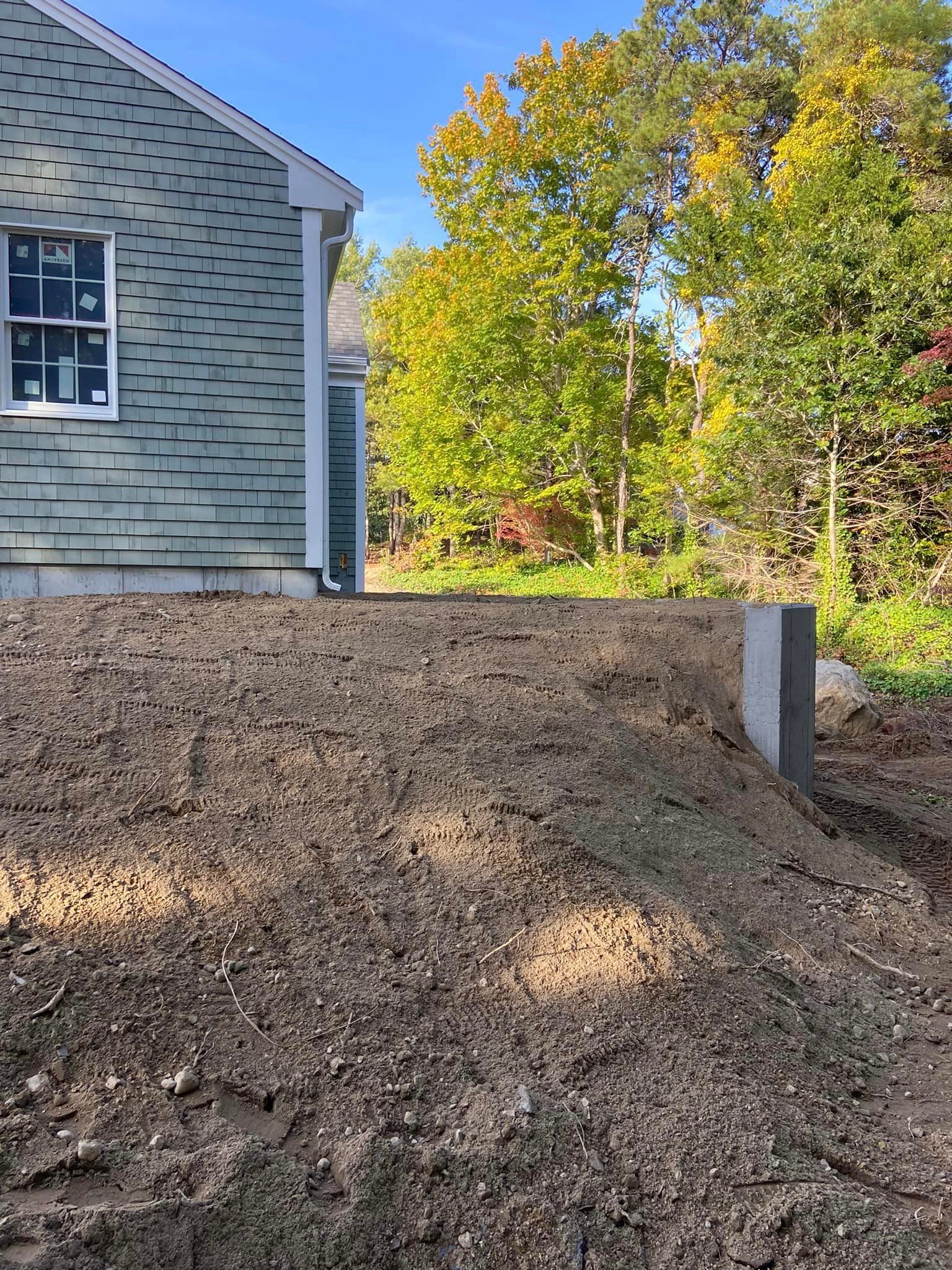 A pile of dirt in front of a house. Trees in the background. Sunny day.
