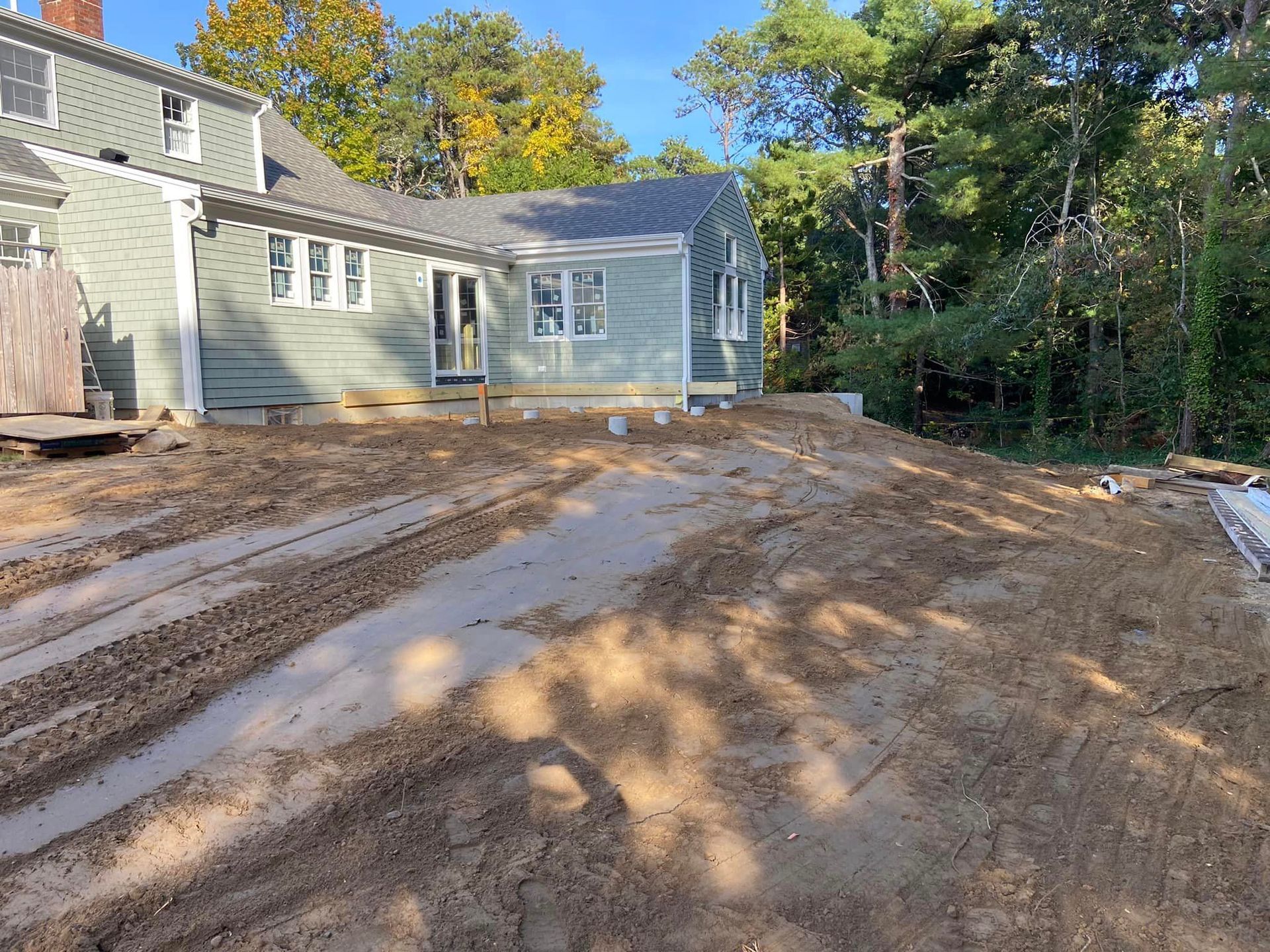 House exterior with construction in progress. Dirt driveway in foreground. Gray siding, white trim.
