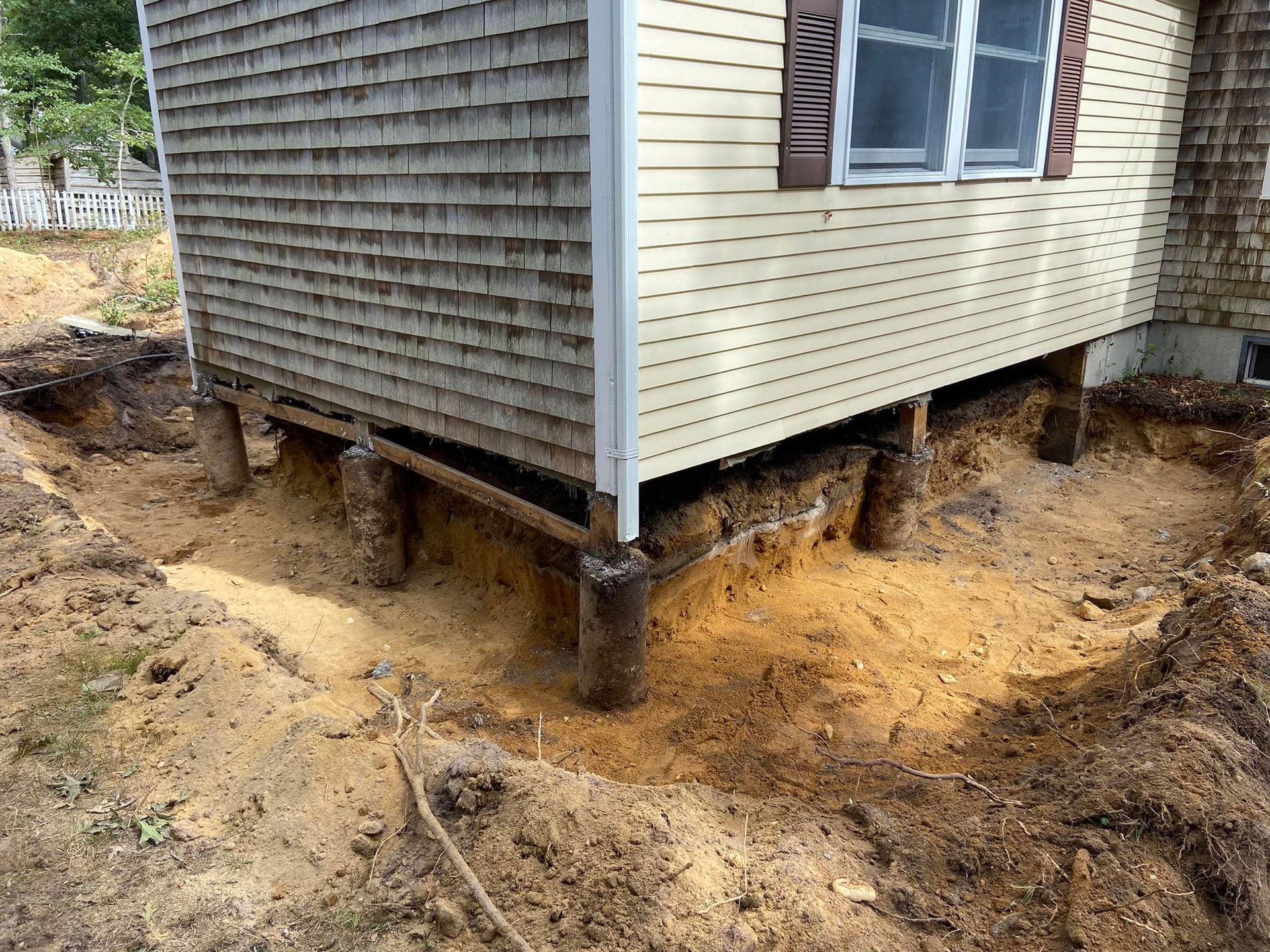 A house raised on wooden pilings, surrounded by a ditch dug in dirt and sand.