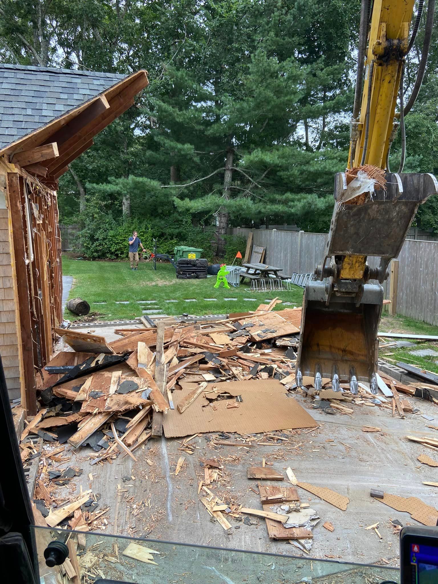 Demolition of a small wooden structure with an excavator. Debris litters the ground.