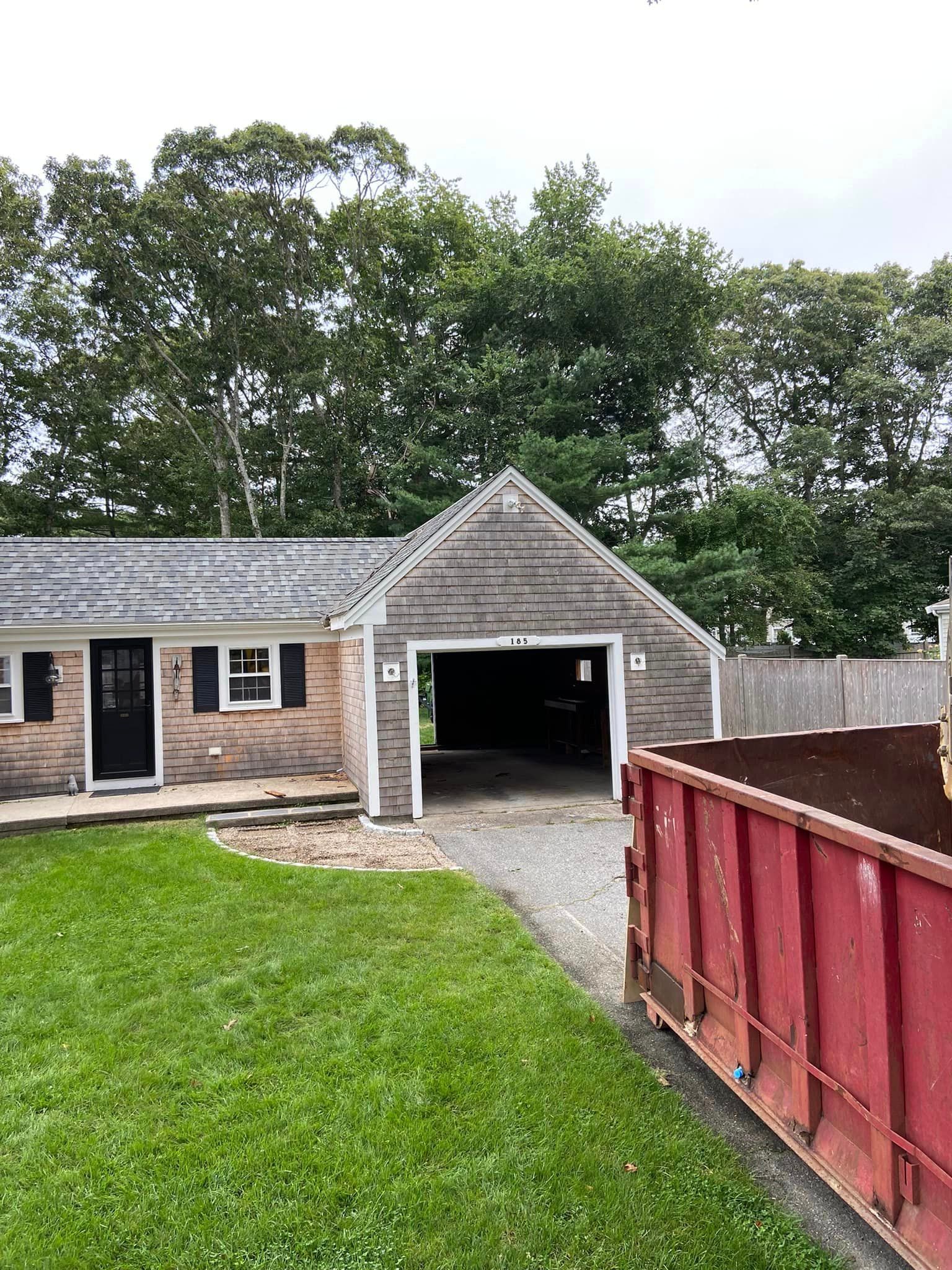 House with garage, green lawn, red dumpster in driveway, trees in background, cloudy sky.