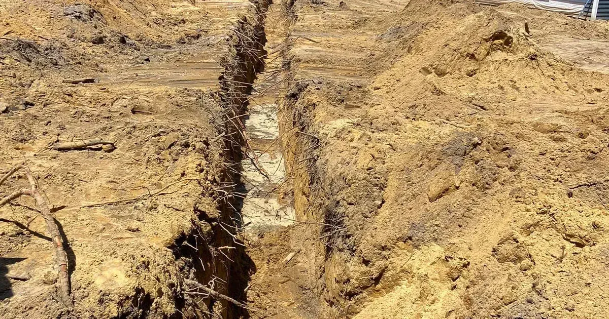 A narrow trench dug in brown soil, with piles of dirt on either side.