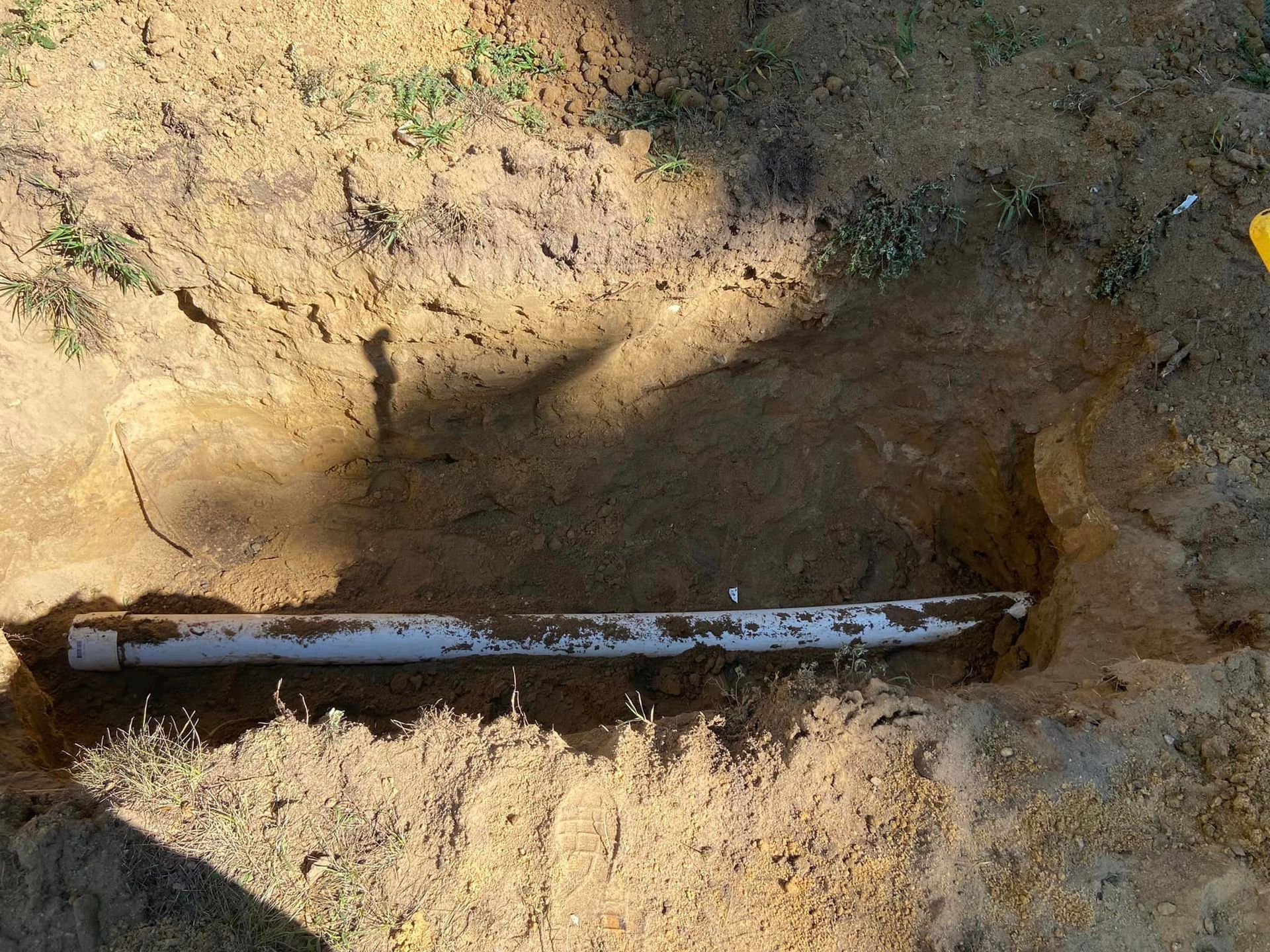 PVC pipe in a dug trench, surrounded by soil and grass.